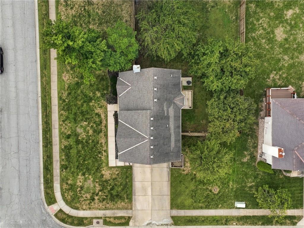 Aerial view of a gray-roofed house with a concrete driveway, lawn, and mature trees.