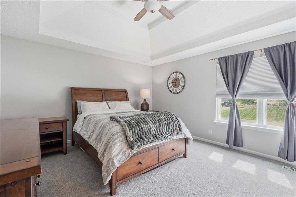 Bedroom with a wooden bed, tray ceiling, and large window framed by gray curtains.