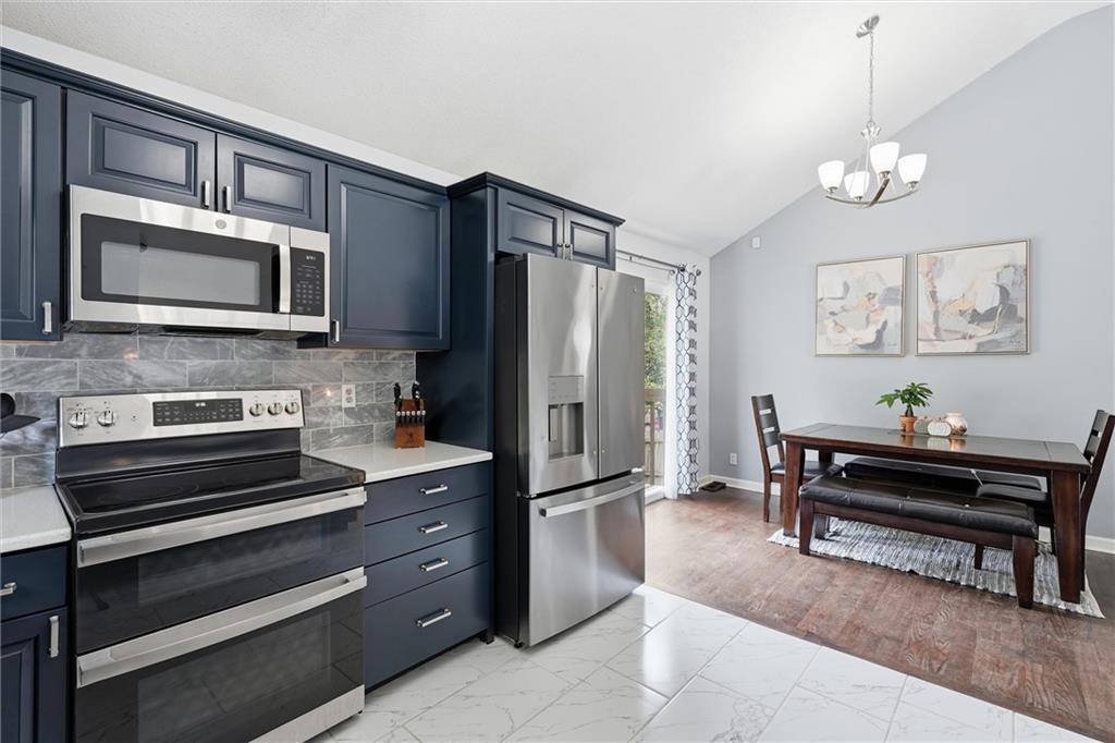 Kitchen with navy cabinets and stainless appliances opening into a dining area with a dark wood table.