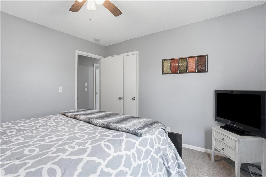 Bedroom with a gray patterned bedspread, ceiling fan, and television.