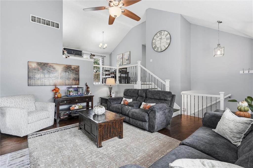 Living room with vaulted ceilings, gray seating, a wood coffee table, and a white-railed staircase.