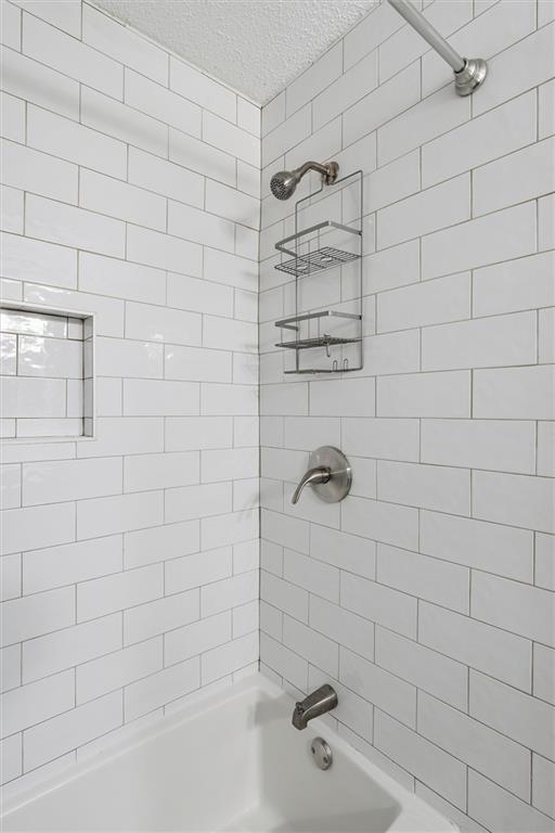 White subway-tile tub and shower with a recessed window and chrome fixtures.
