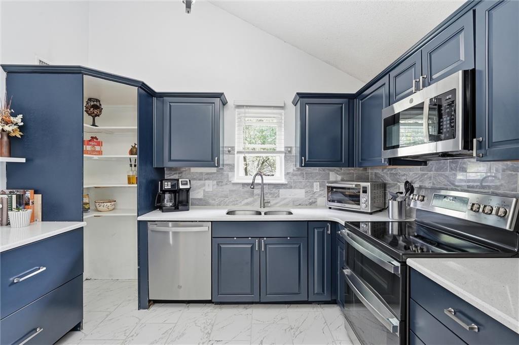 Kitchen with navy cabinets, a marble-look backsplash, stainless appliances, and a double-basin sink.