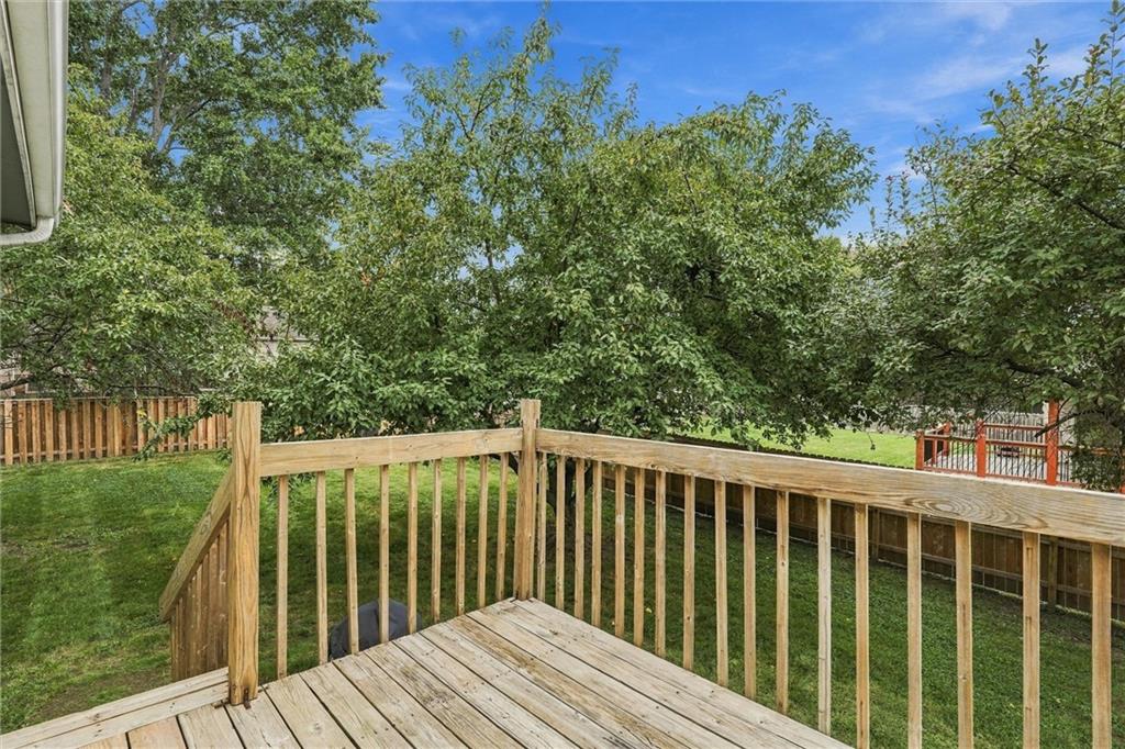 Backyard deck with wooden railings overlooking a fenced, tree-shaded lawn.