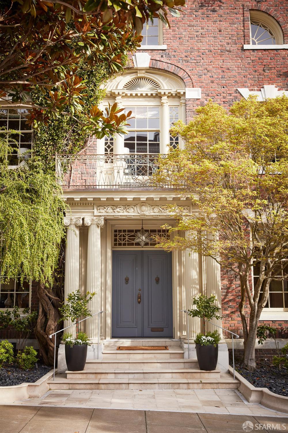 Brick building entrance with ornate stonework, gray double doors, and landscaped steps.