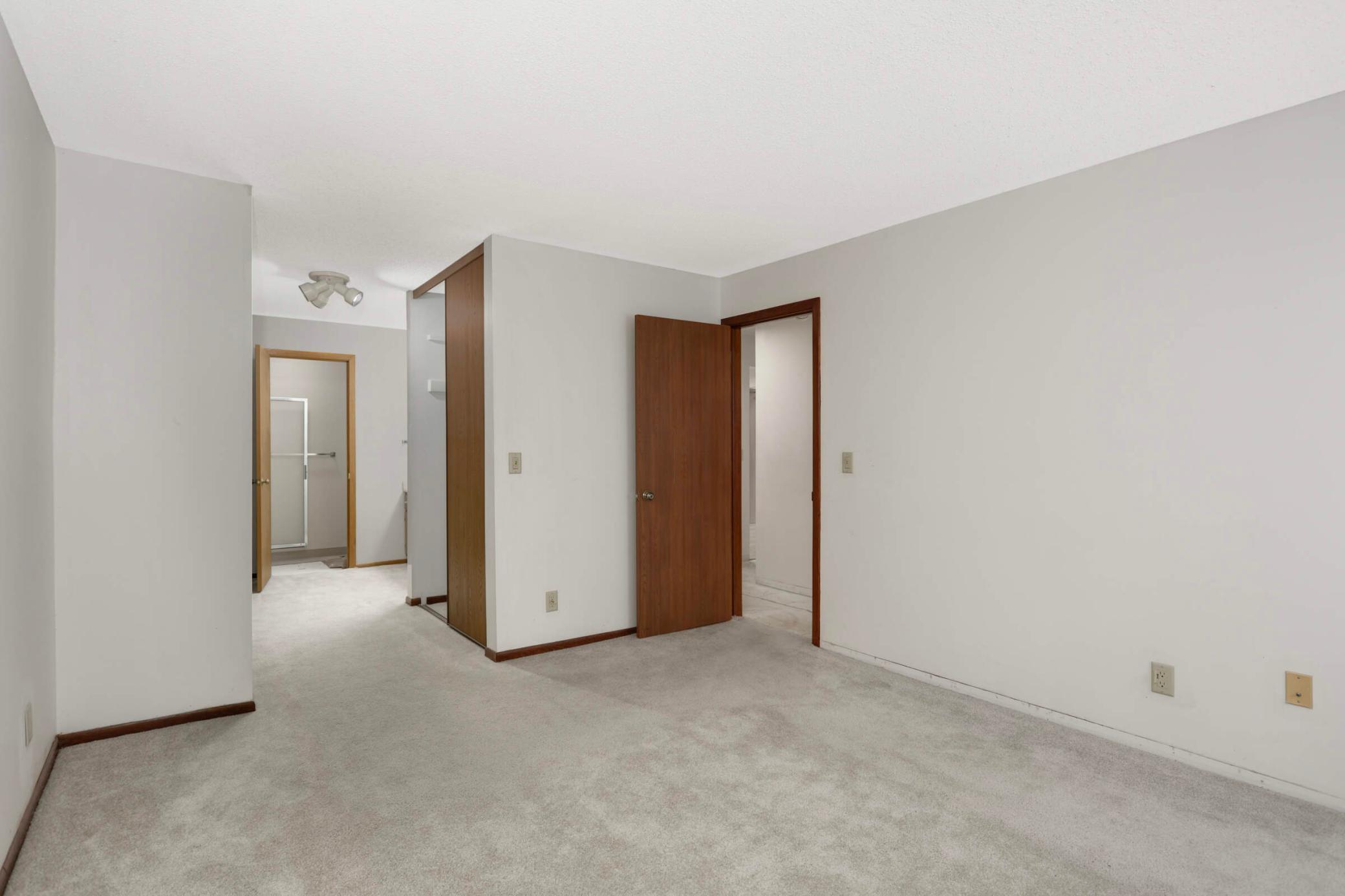 Vacant bedroom with light carpeting, wood-trimmed doors, and a bathroom doorway.