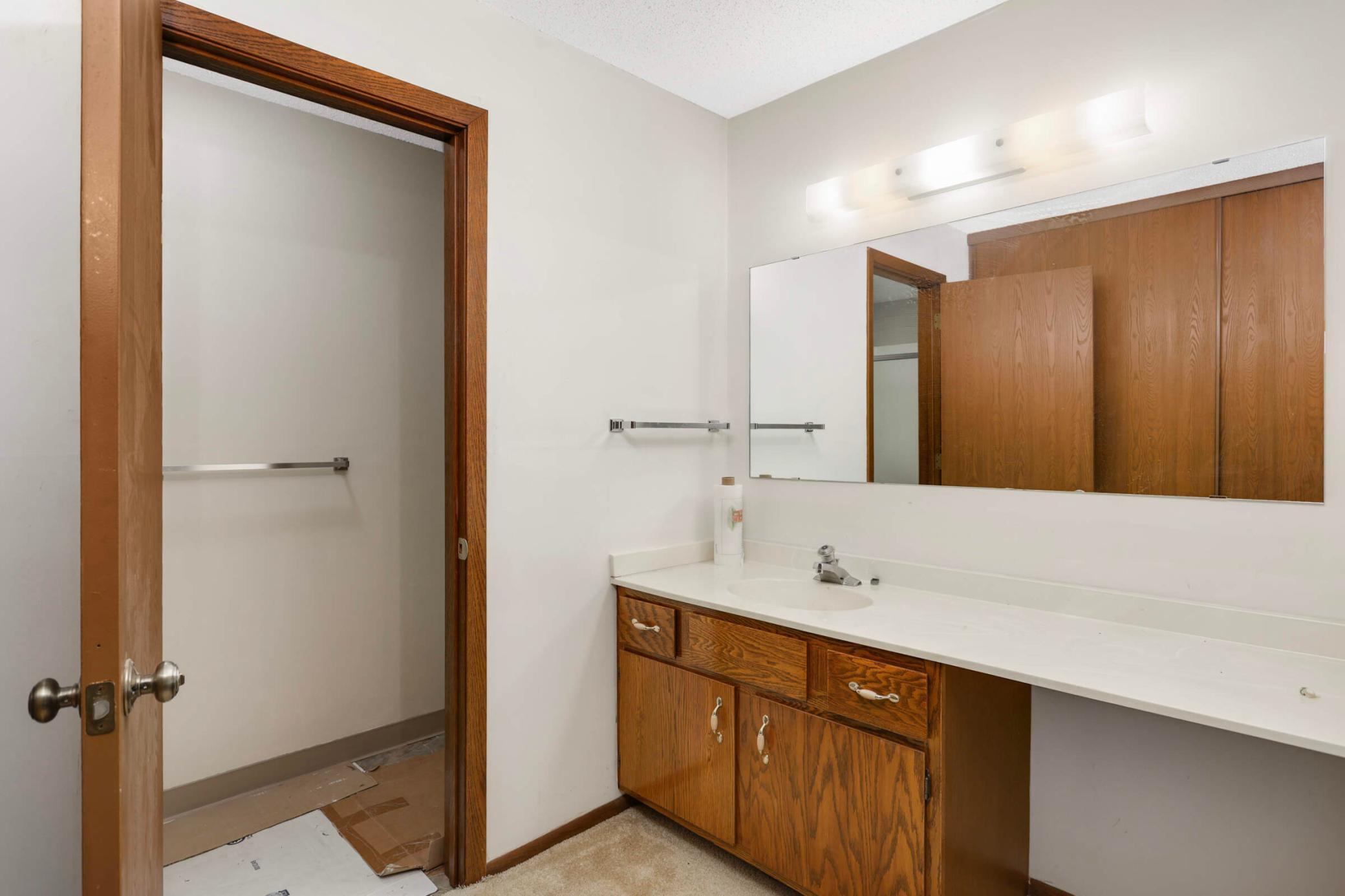 Bathroom with a long white vanity, wood cabinets, and a large mirror.
