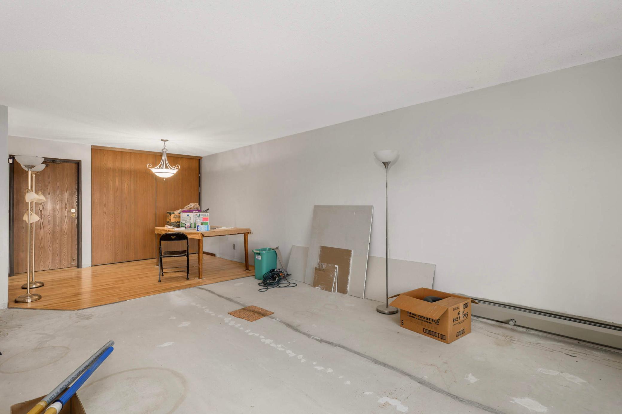 Mostly empty condo living area with unfinished concrete flooring, renovation supplies, and a strip of hardwood.