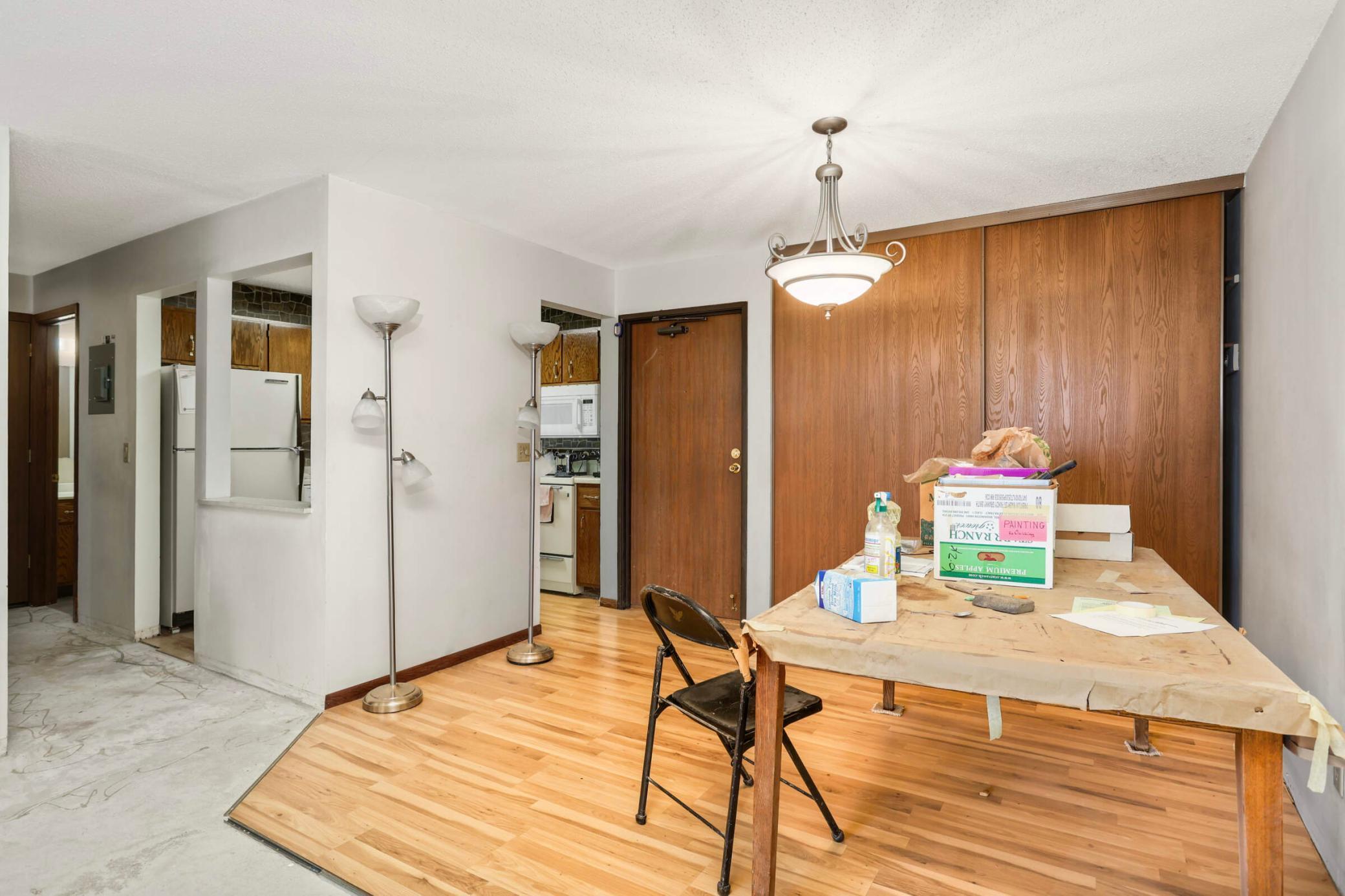 Dining area with hardwood floors, a wood-paneled wall, and a paper-covered table beside the kitchen.