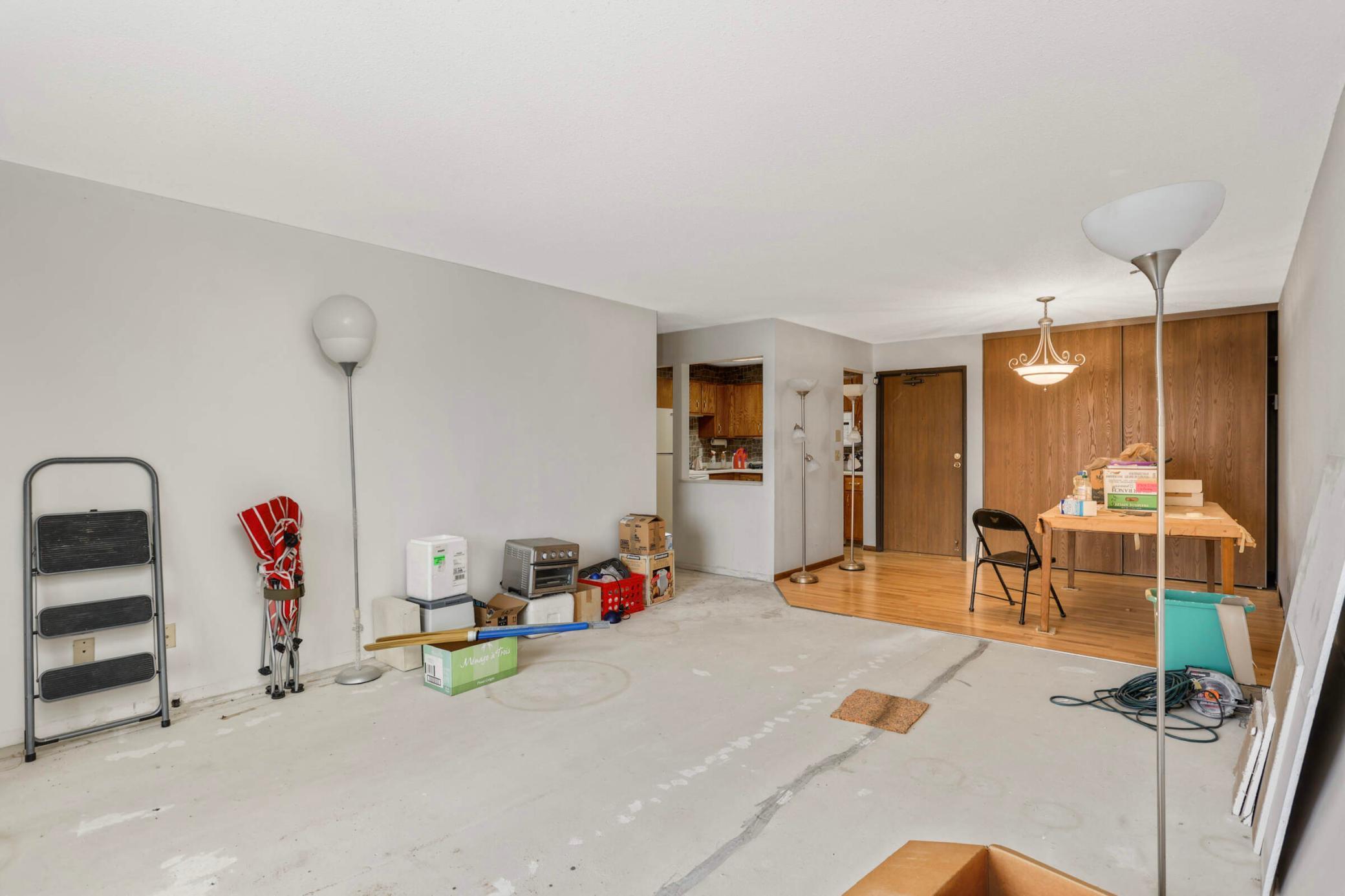 Condo living and dining area with a bare concrete floor, boxes, and a wood-paneled wall.