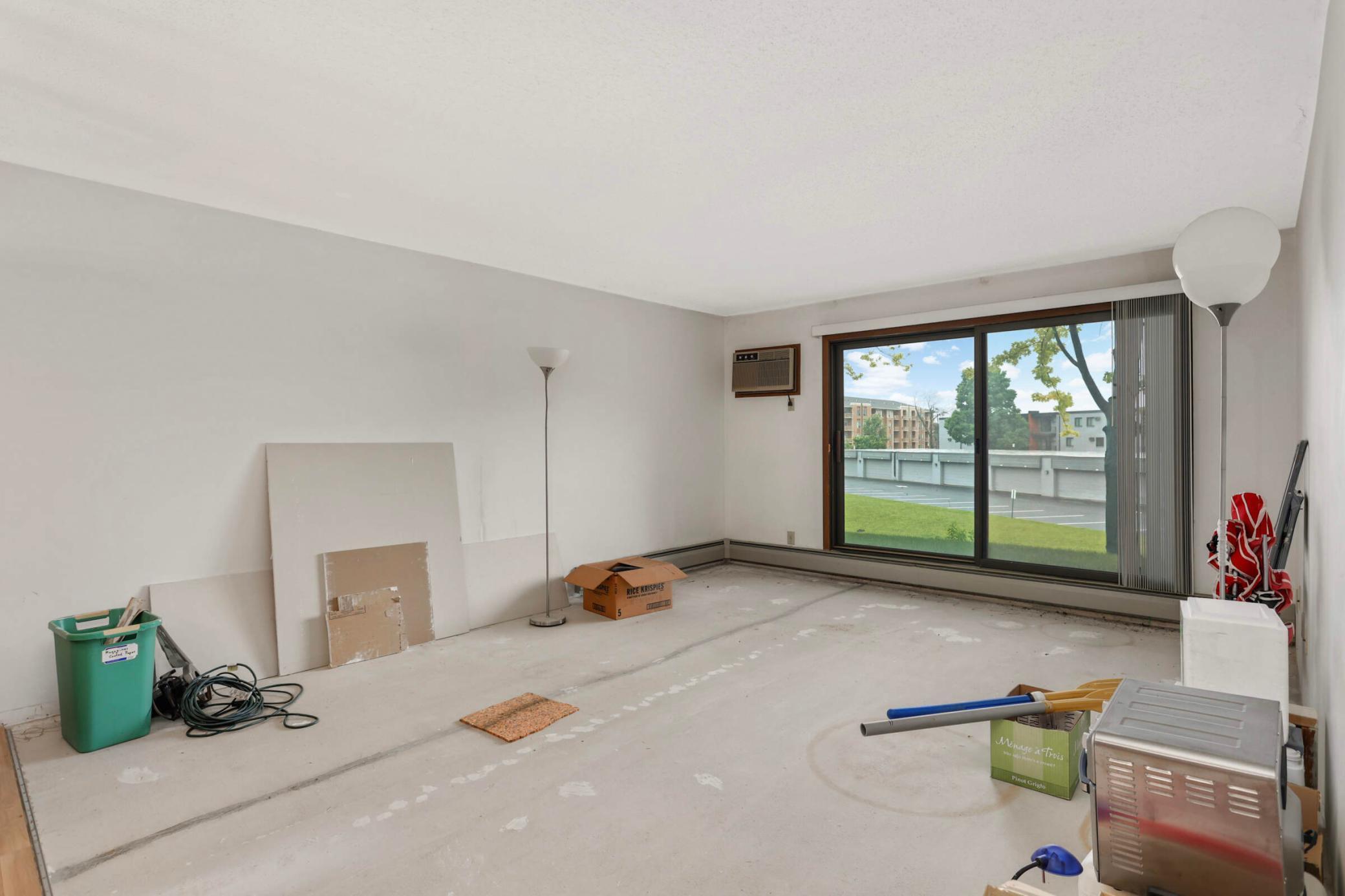 Vacant condo living room with sliding glass doors overlooking a grassy area and parking lot.