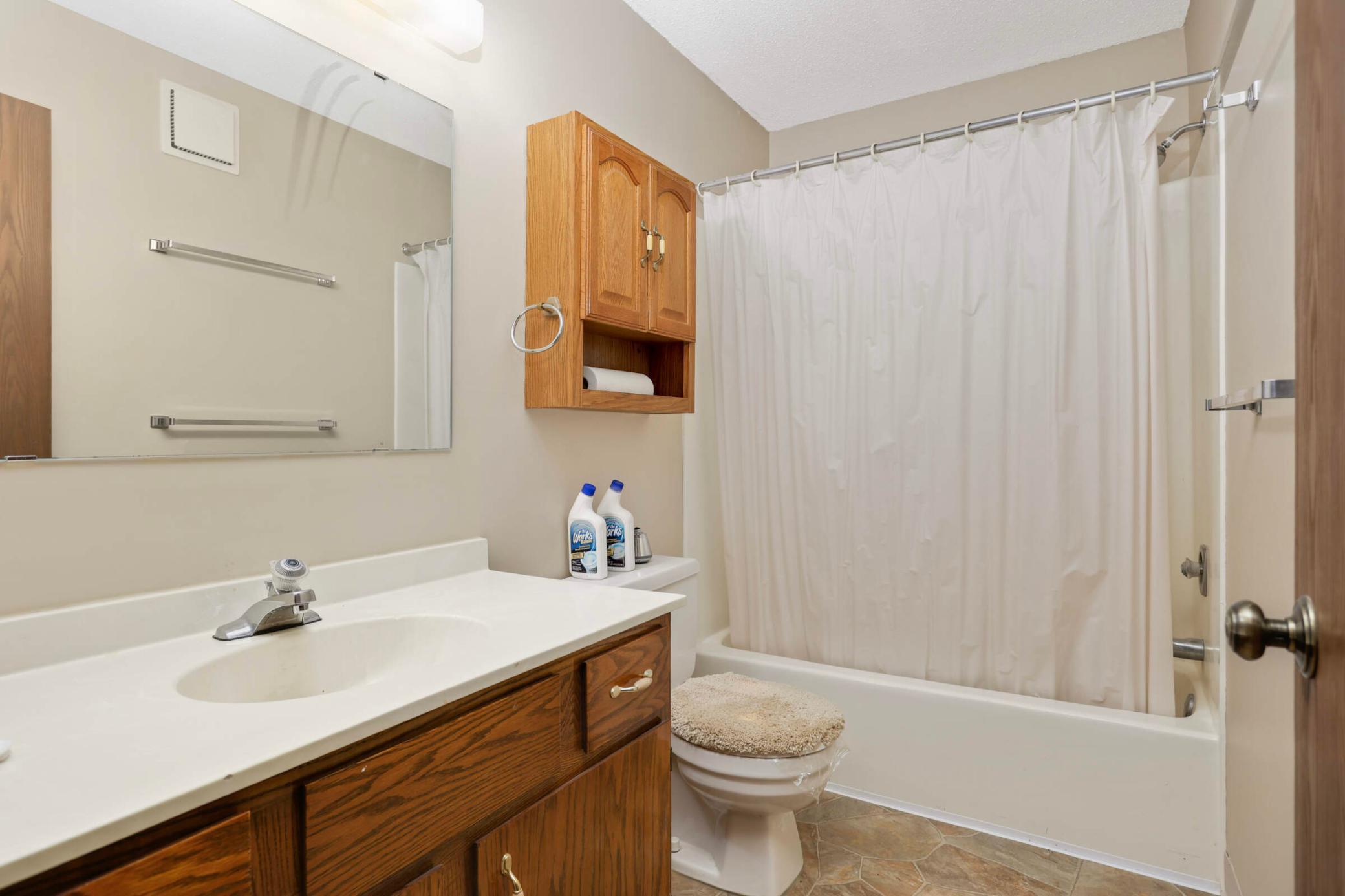 Bathroom with dark wood vanity, large mirror, and bathtub behind a white shower curtain.