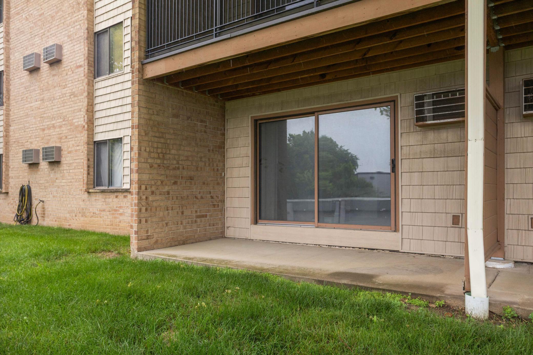Covered condominium patio with a sliding glass door and lawn in front.