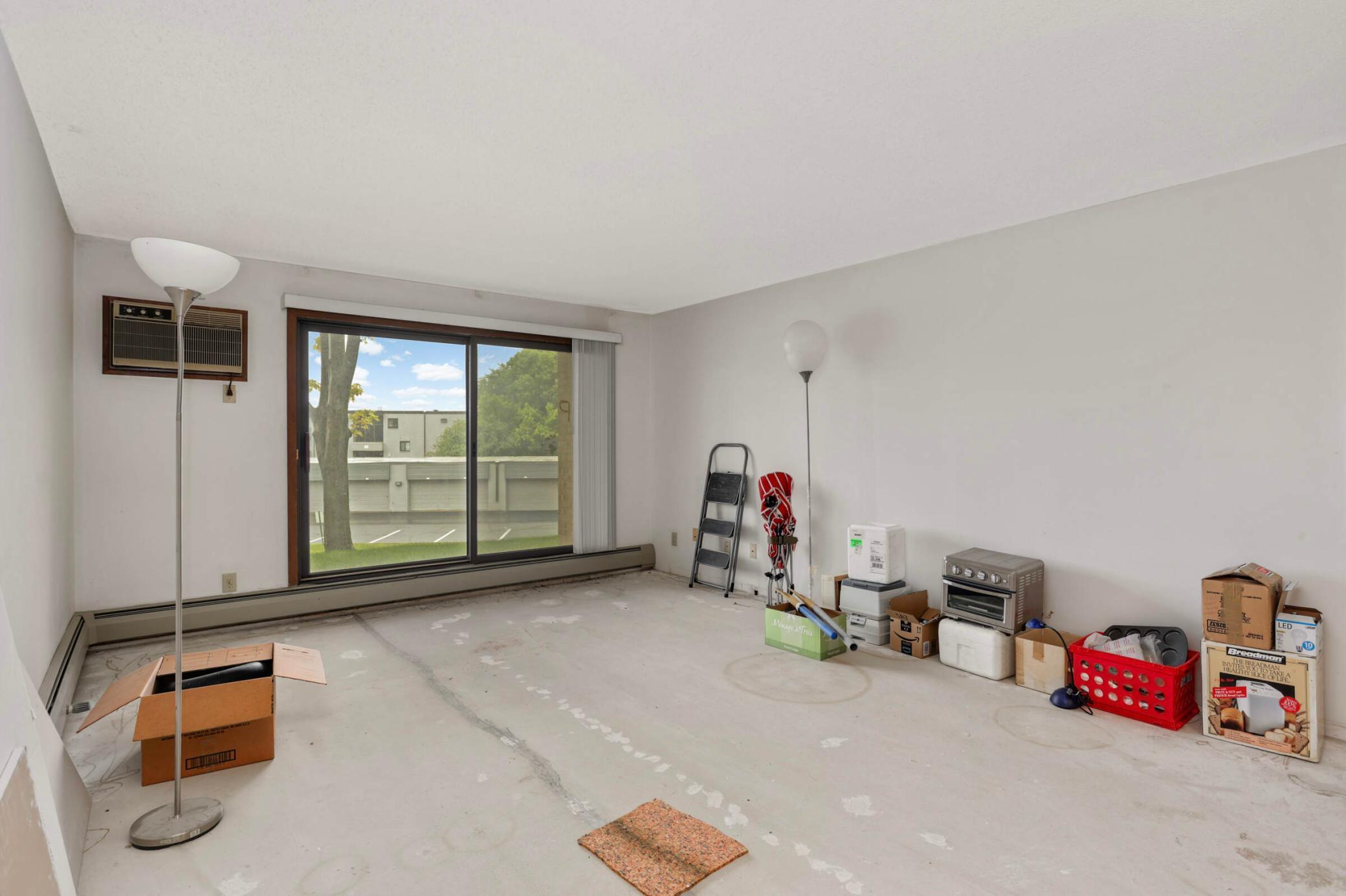 Living room with a sliding glass door, bare concrete floor, and boxes and appliances along one wall.