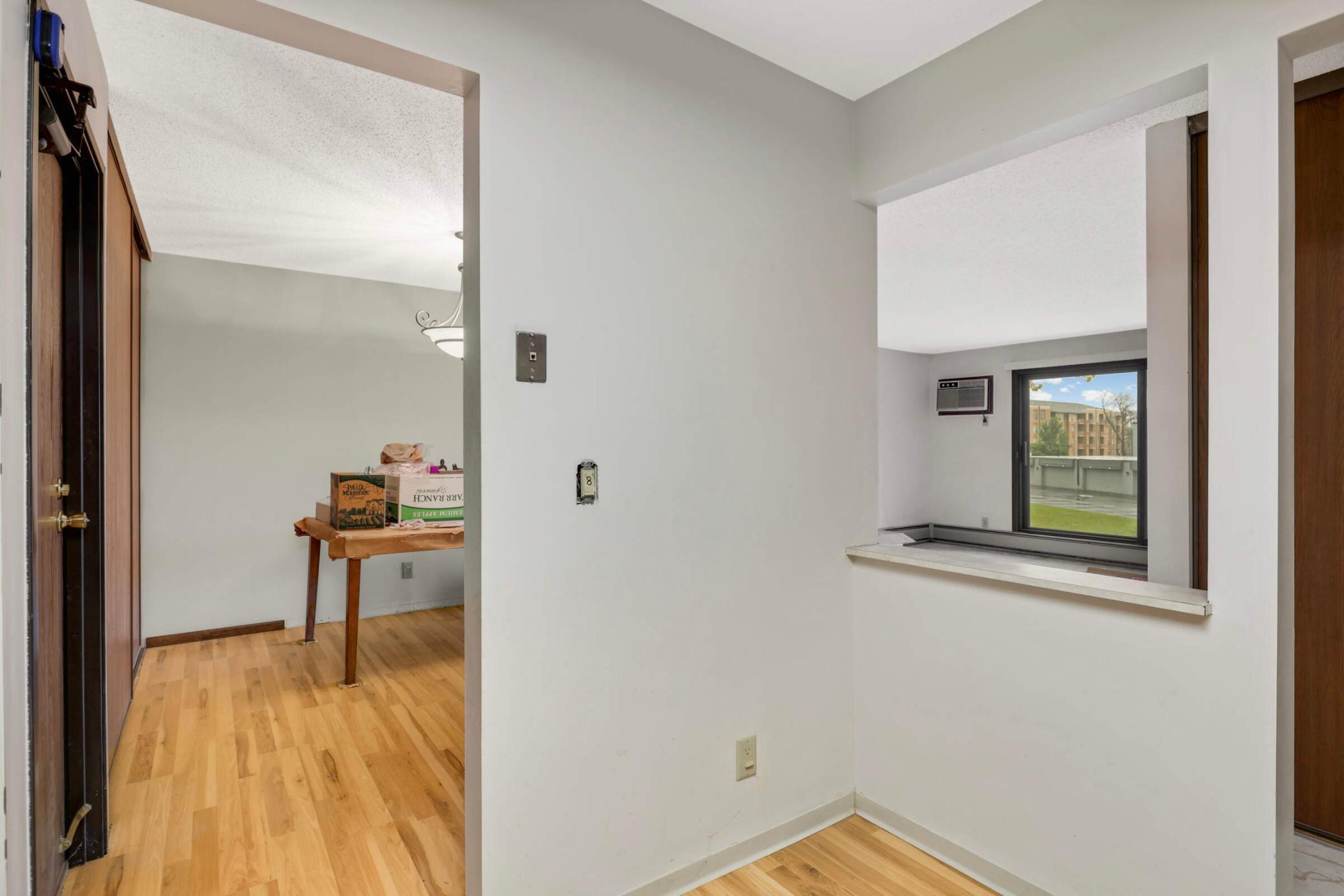 Condo entry and dining area with light wood floors and a pass-through to a windowed room.