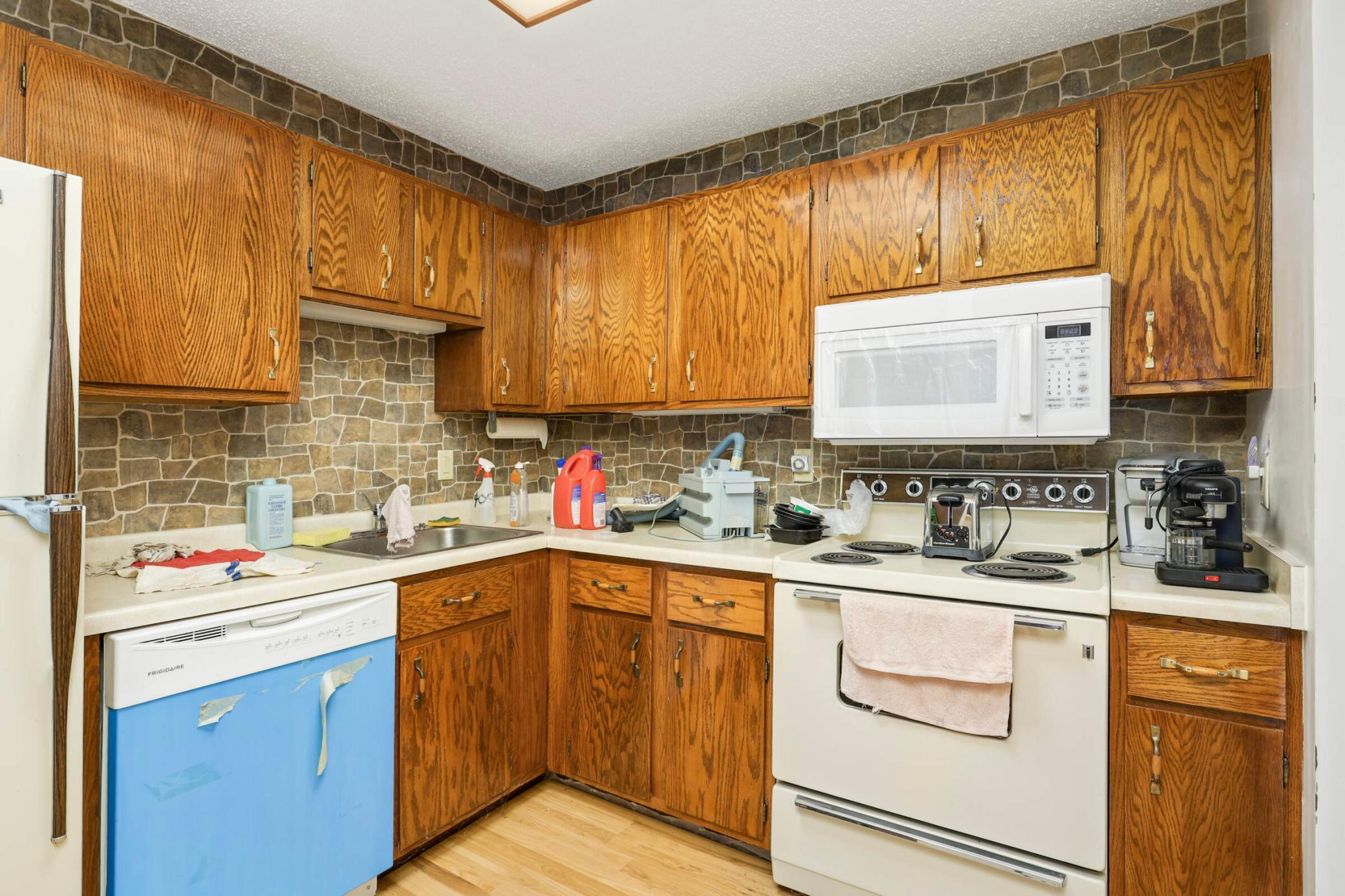 Kitchen with honey-colored wood cabinets, stone-pattern backsplash, and a blue-front dishwasher.