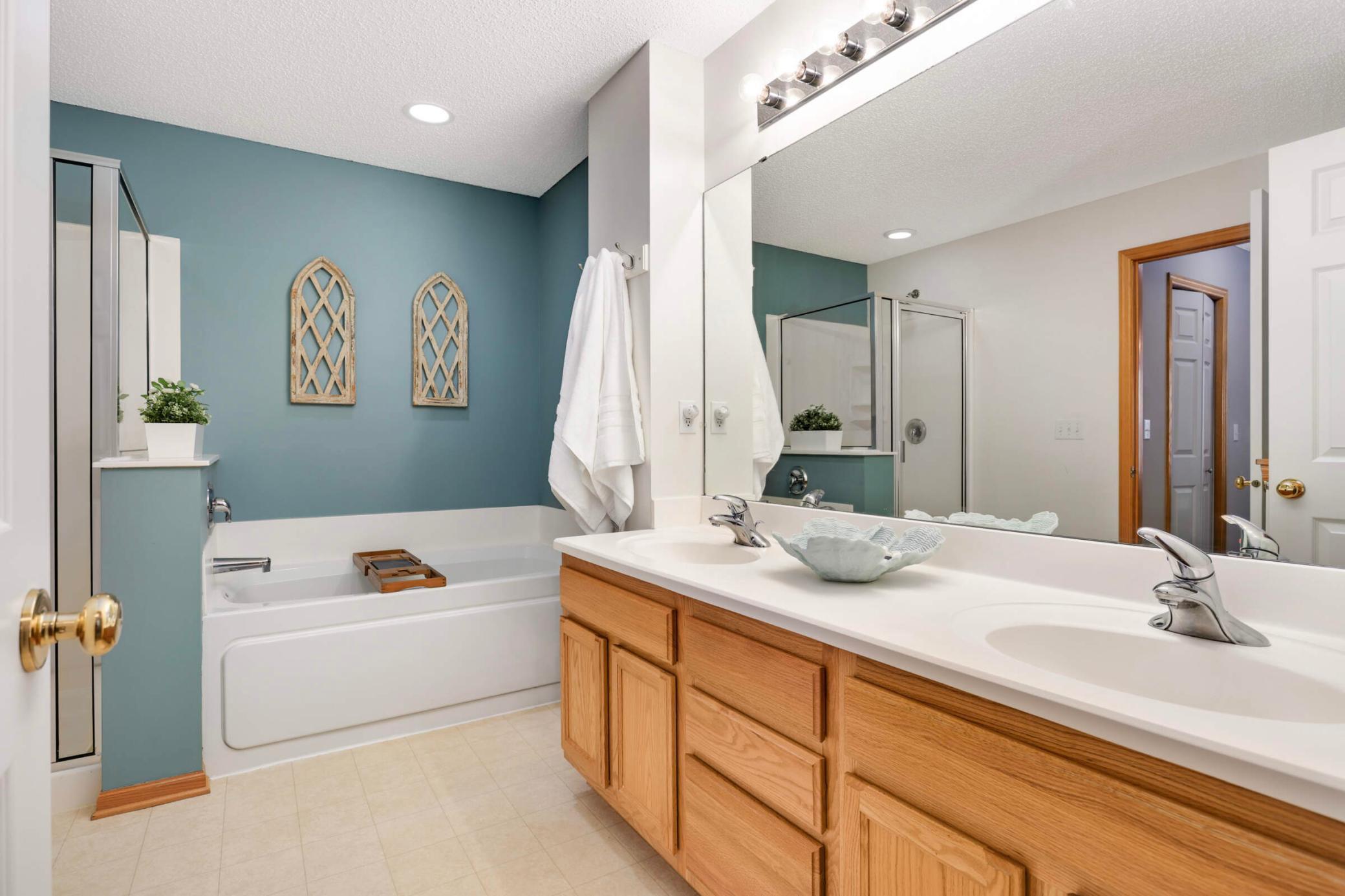 Bathroom with a white soaking tub, glass shower, and oak double-sink vanity.