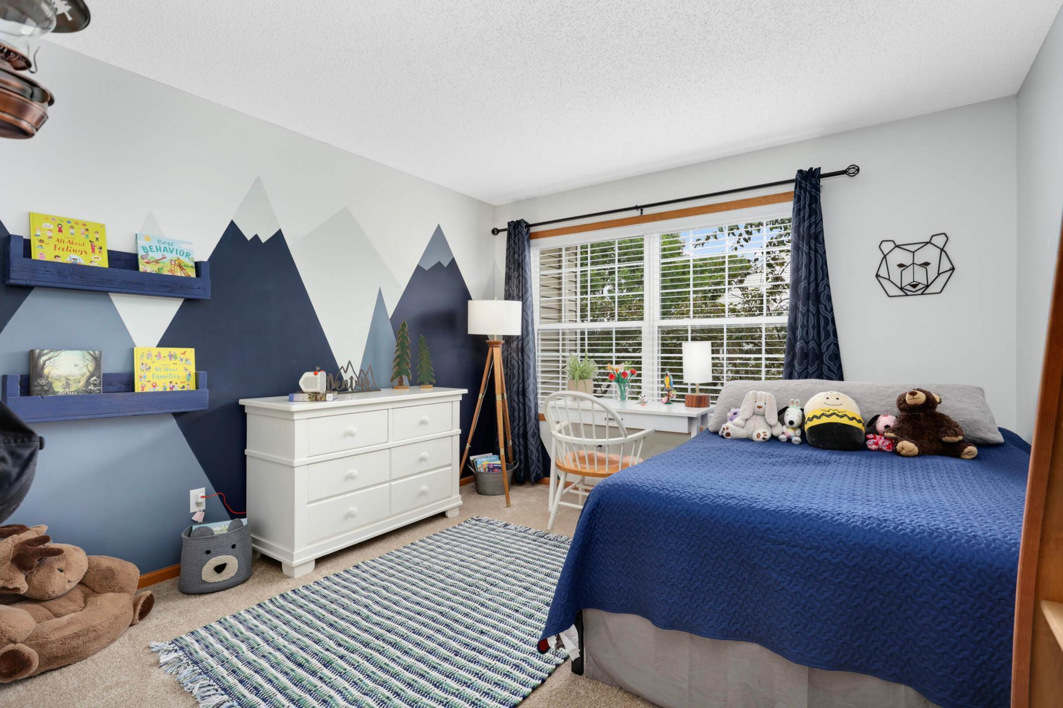 Child’s bedroom with a blue bed, stuffed animals, and a geometric mountain mural.