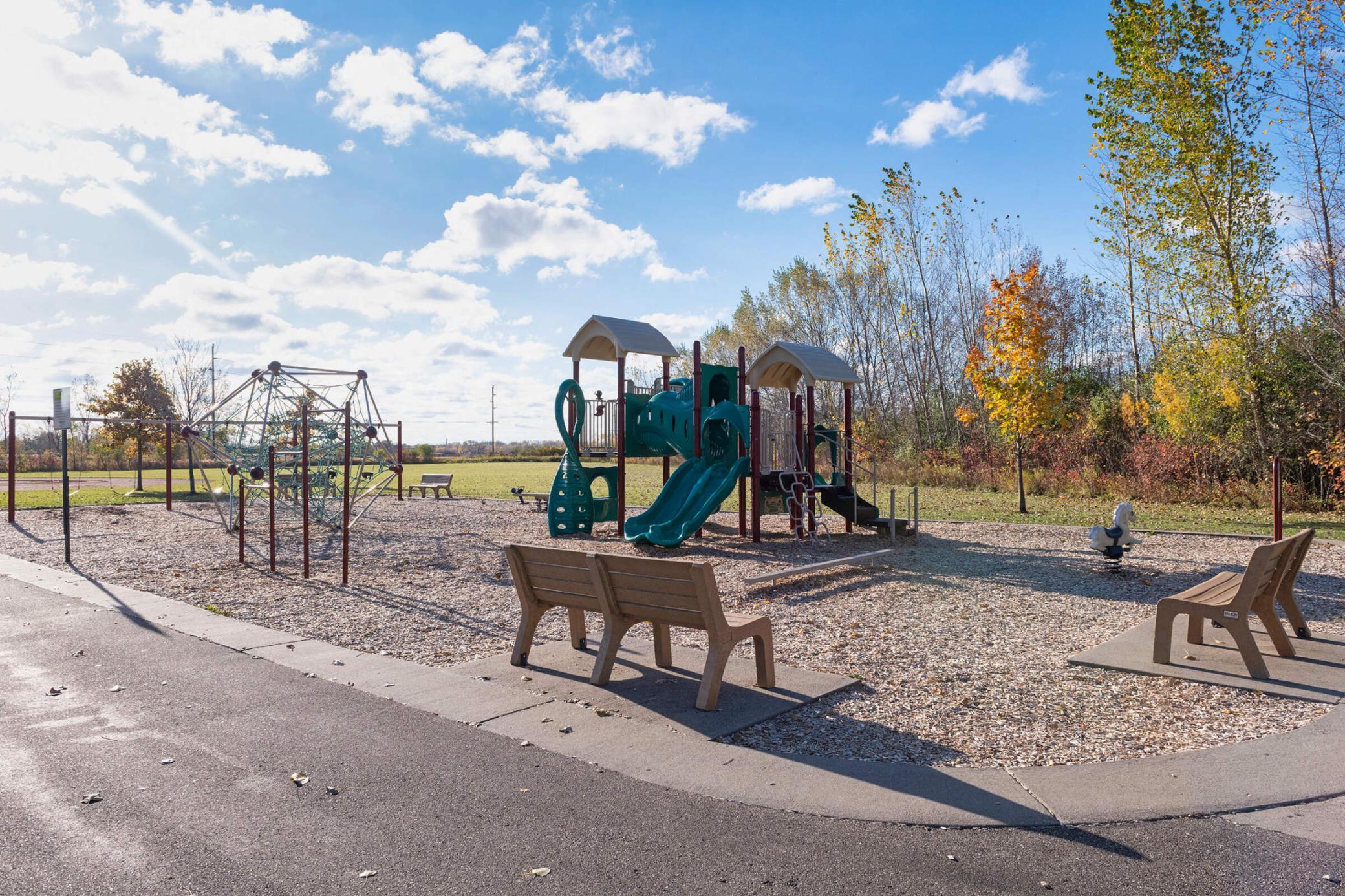 Community playground with teal slides, a climbing structure, and benches among autumn trees.