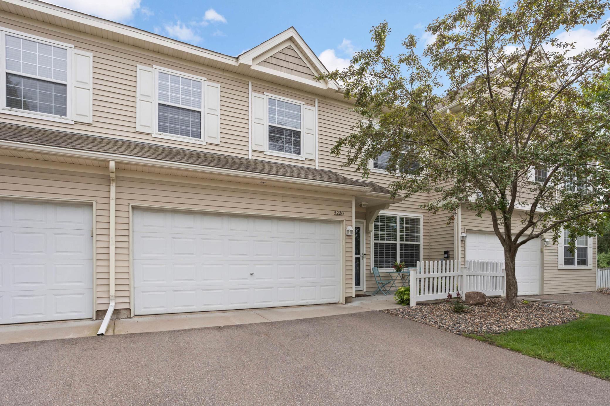 Beige townhouse exterior with white garage doors, a fenced patio, and a mature tree.