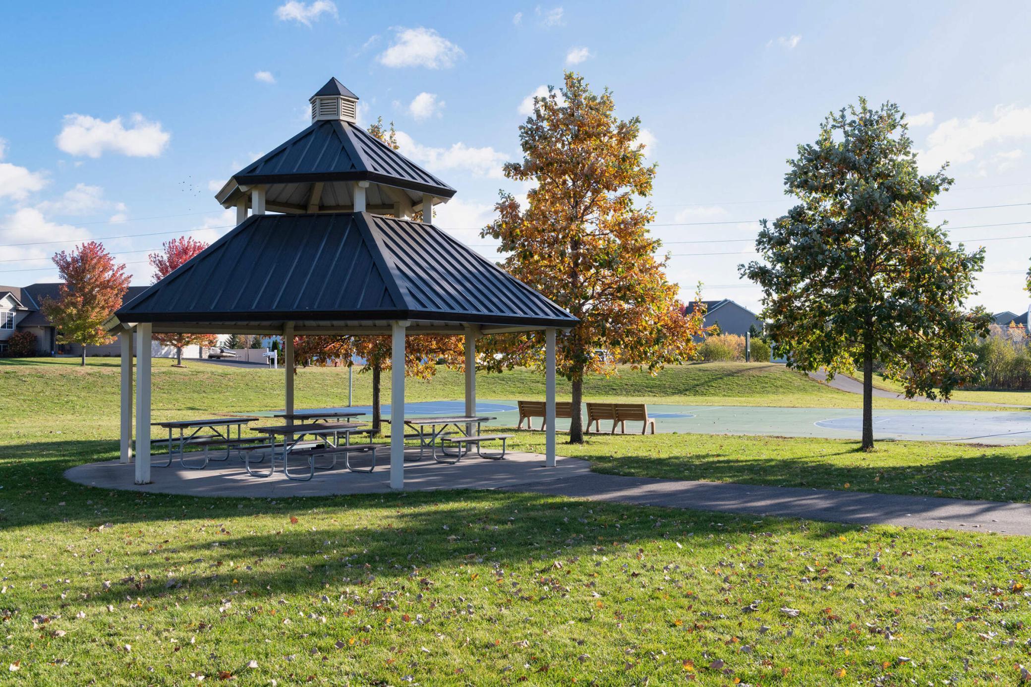 Neighborhood pavilion with picnic tables beside a basketball court and autumn trees.