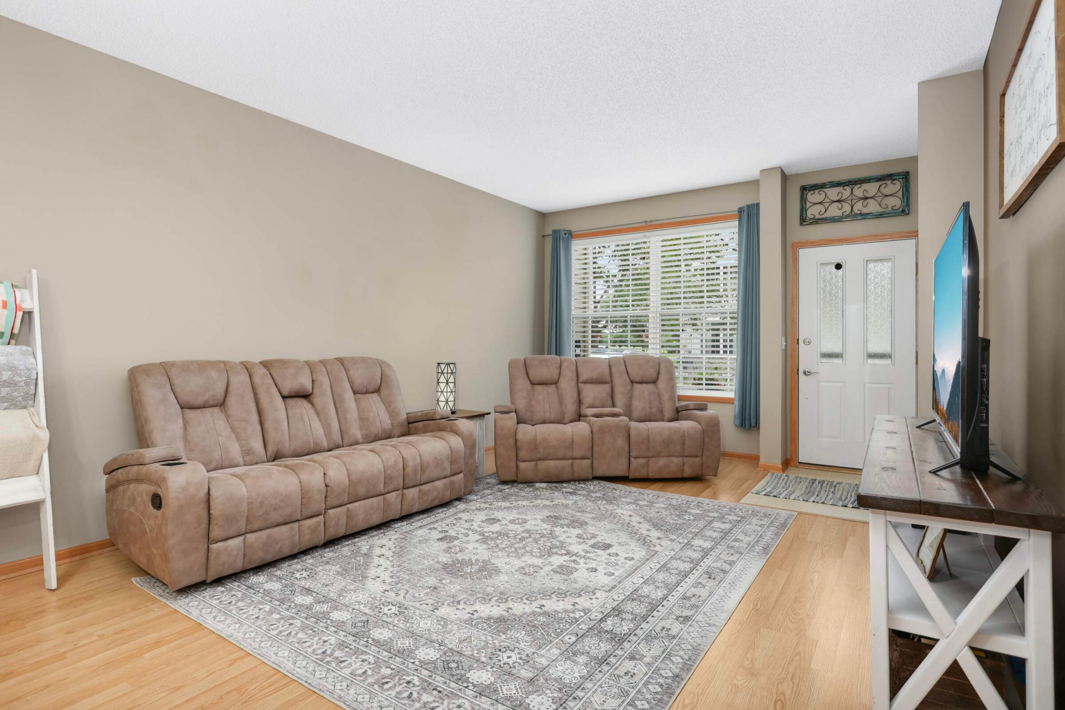 Living room with two tan reclining sofas, a patterned rug, and a television by the entry door.