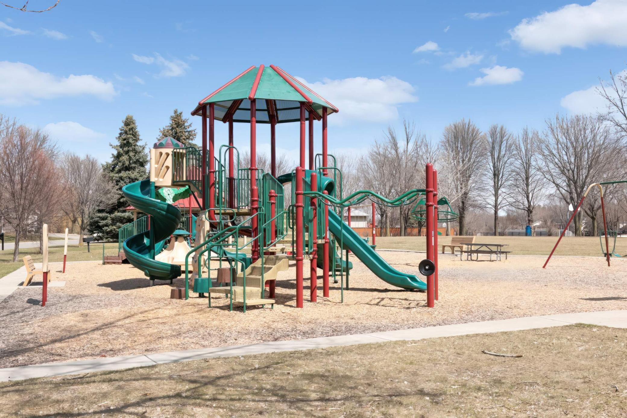 Neighborhood playground with a large climbing structure, spiral slide, straight slide, and swings.