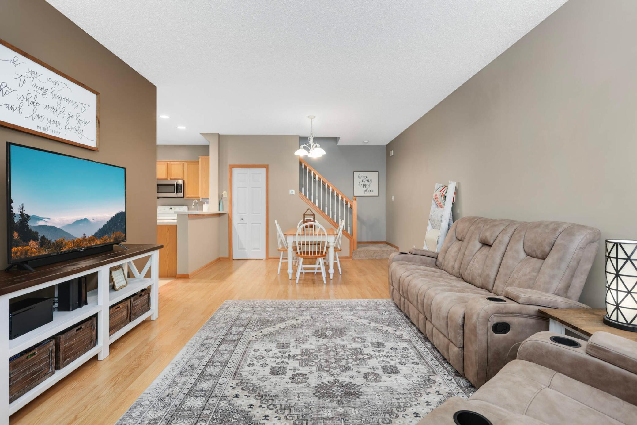 Furnished living room with a taupe reclining sectional, patterned rug, dining area, and staircase.