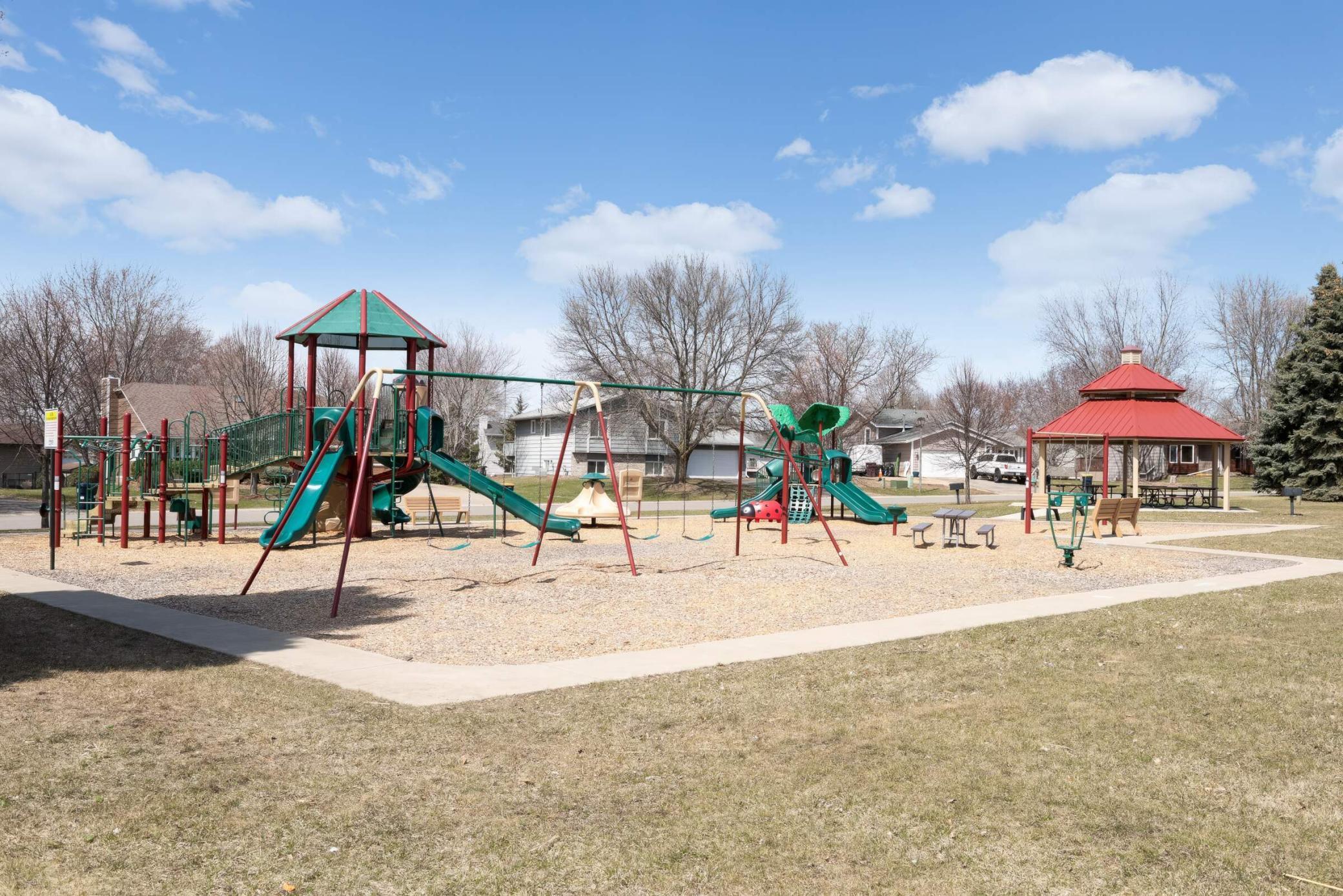 Community playground with colorful slides and swings beside a red-roofed gazebo.