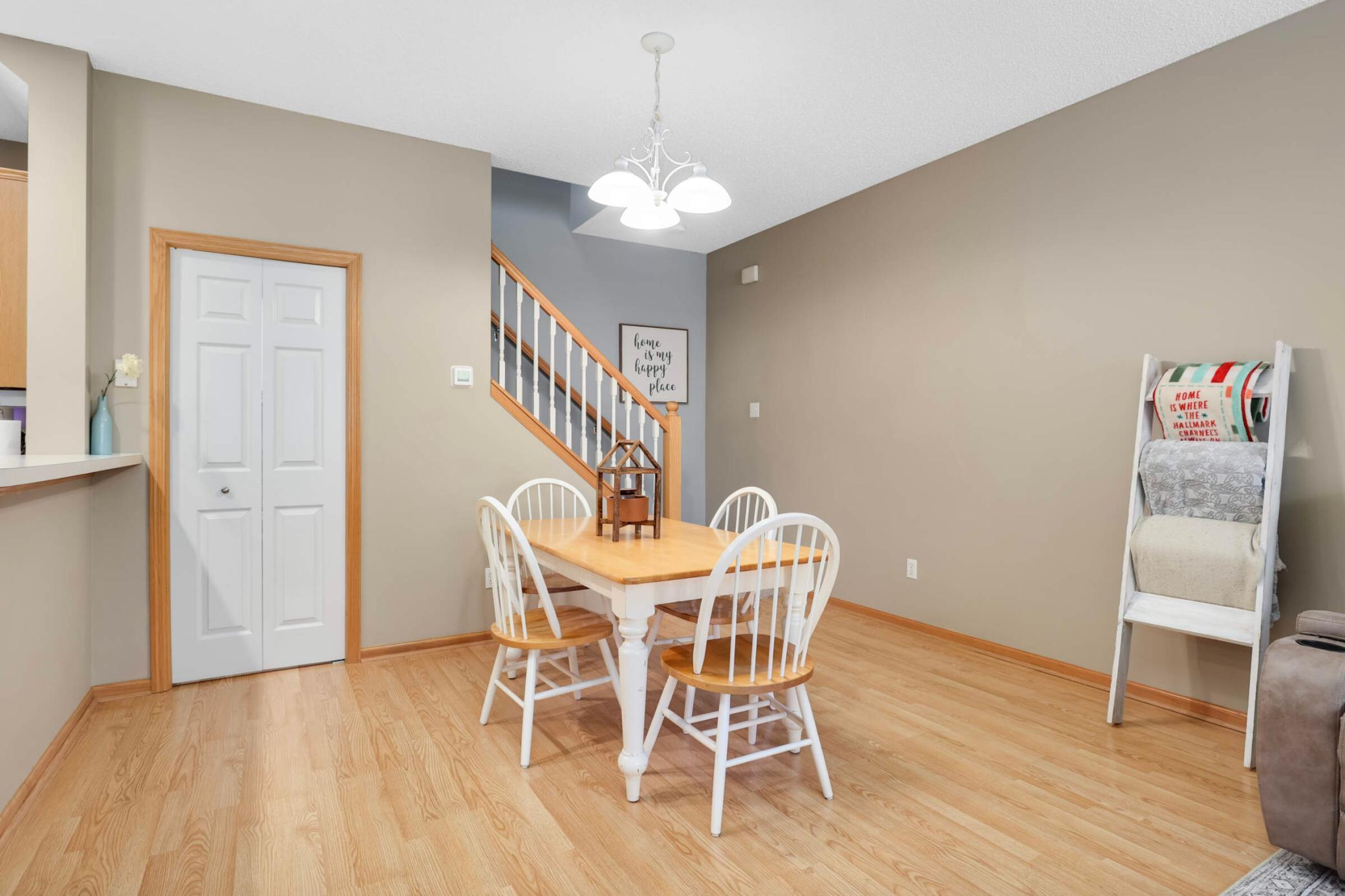 Dining area with a light wood table, white chairs, hardwood floors, and a staircase with wood railings.