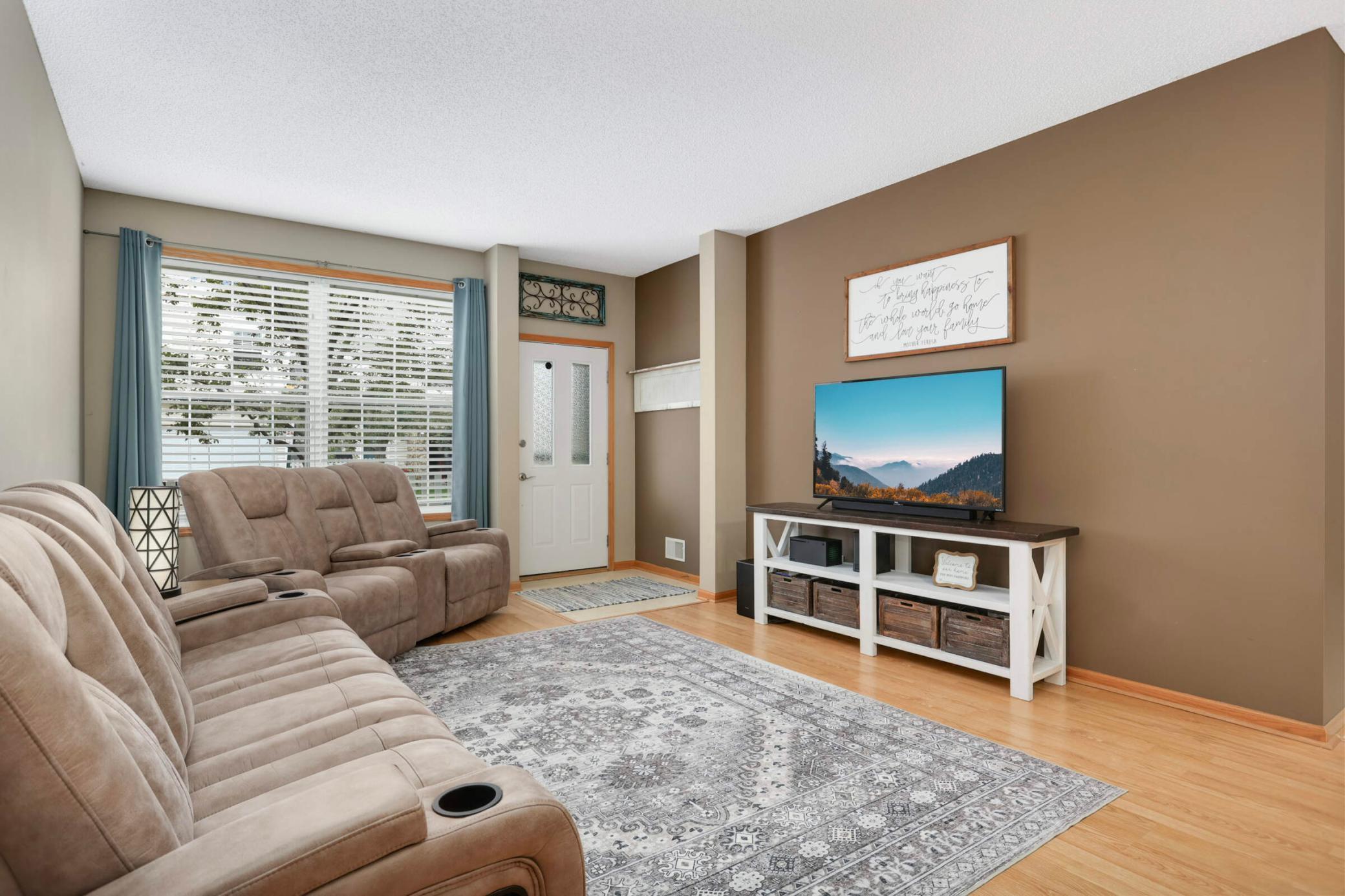 Living room with beige reclining sofas, a patterned rug, and a television on a console.