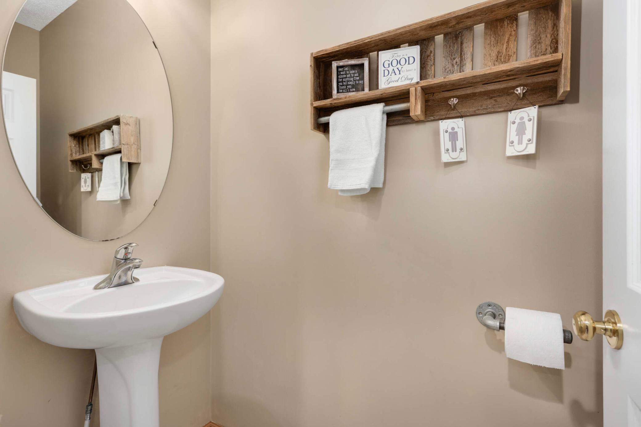 Bathroom with a white pedestal sink, oval mirror, and rustic wooden towel shelf.