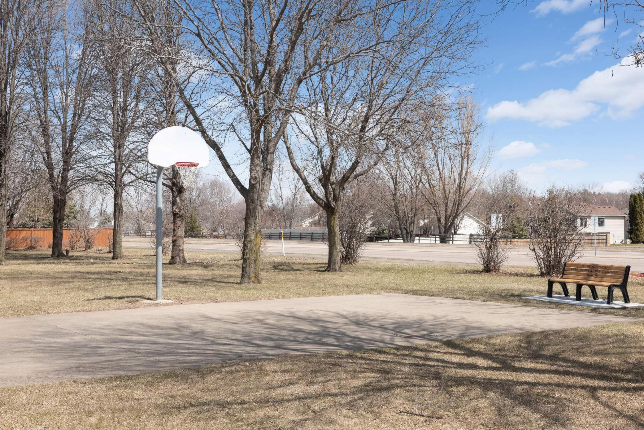 Outdoor basketball court with a single hoop and a bench beside leafless trees.