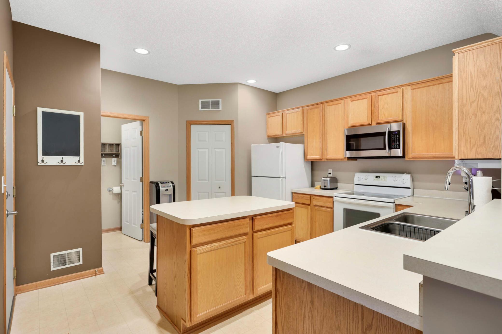 Kitchen with honey-colored cabinets, central island, white appliances, and a double-sink peninsula.