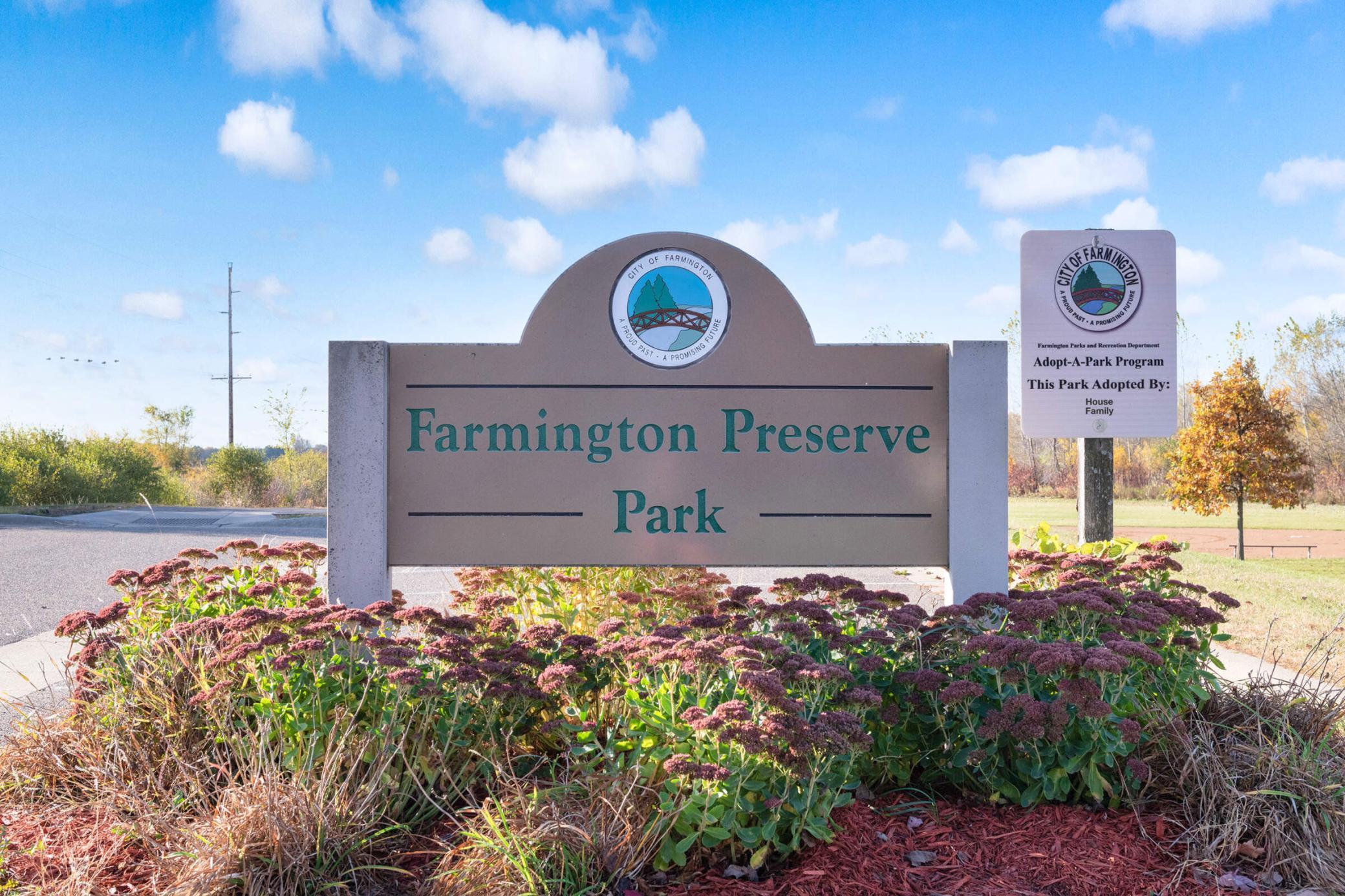 Farmington Preserve Park entrance sign among flower beds, with an Adopt-A-Park sign nearby.
