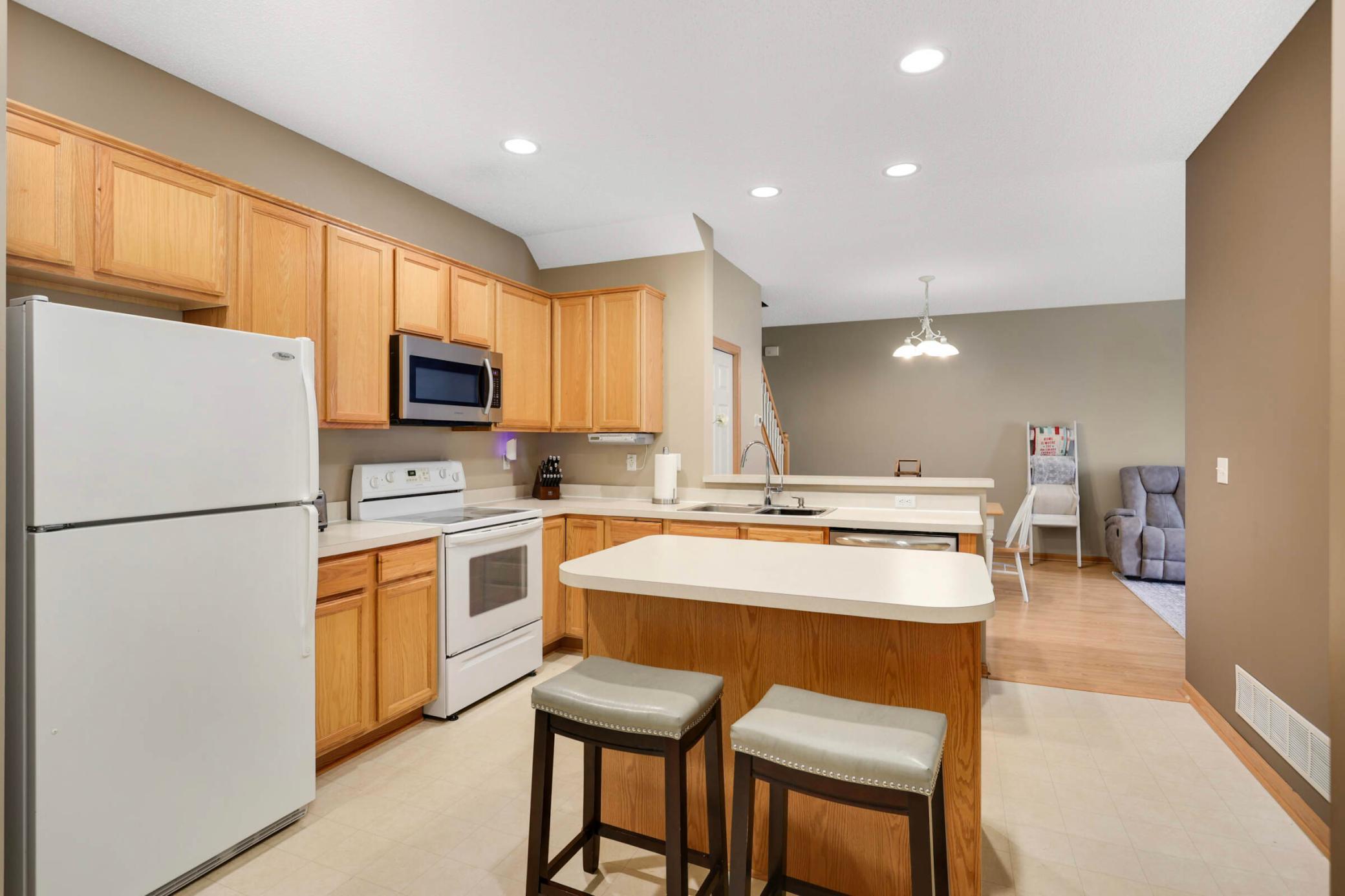 Kitchen with light wood cabinets, white appliances, and an island with two stools.