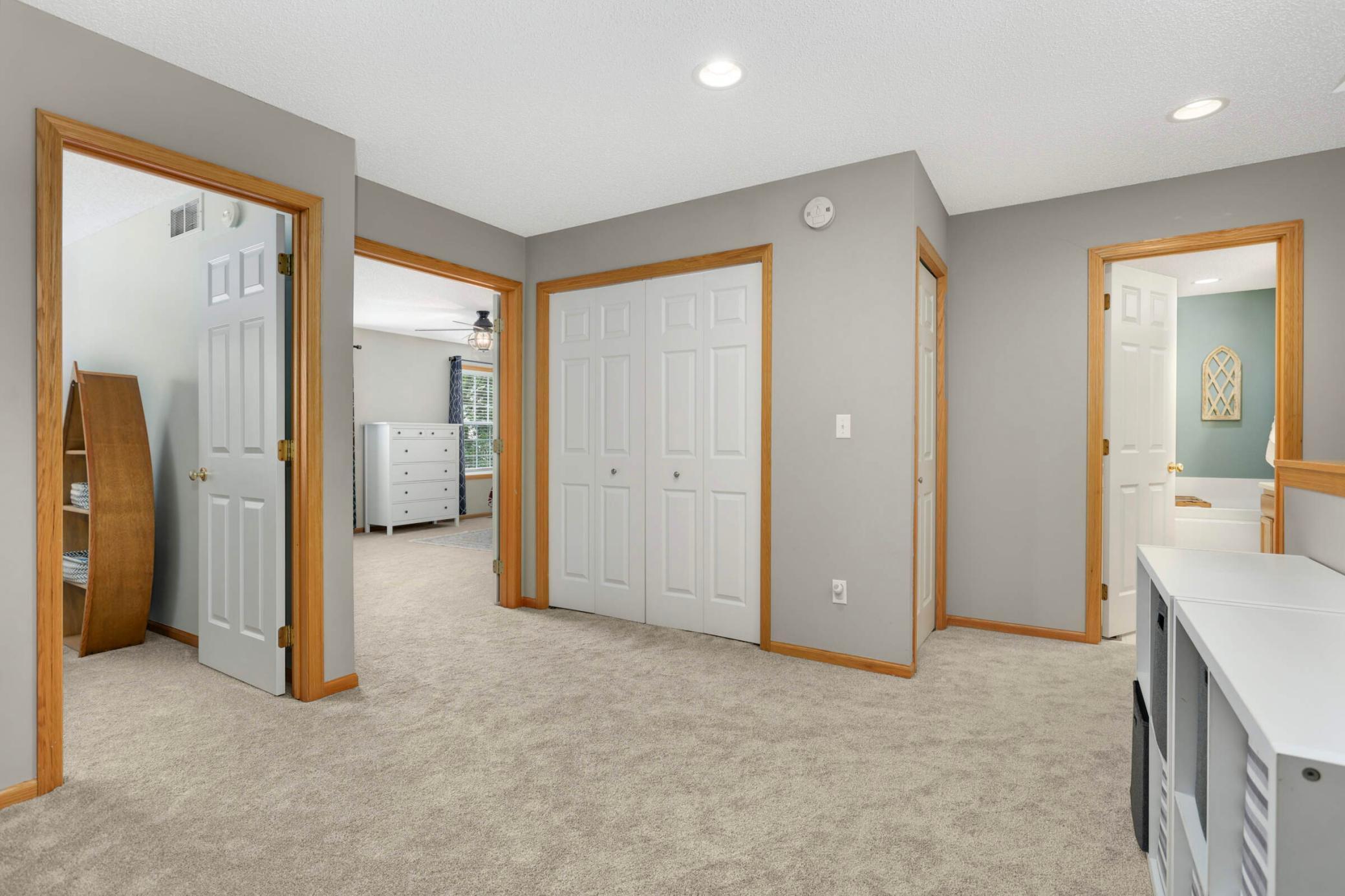 Carpeted landing with white closet doors and open doorways to a bedroom and bathroom.