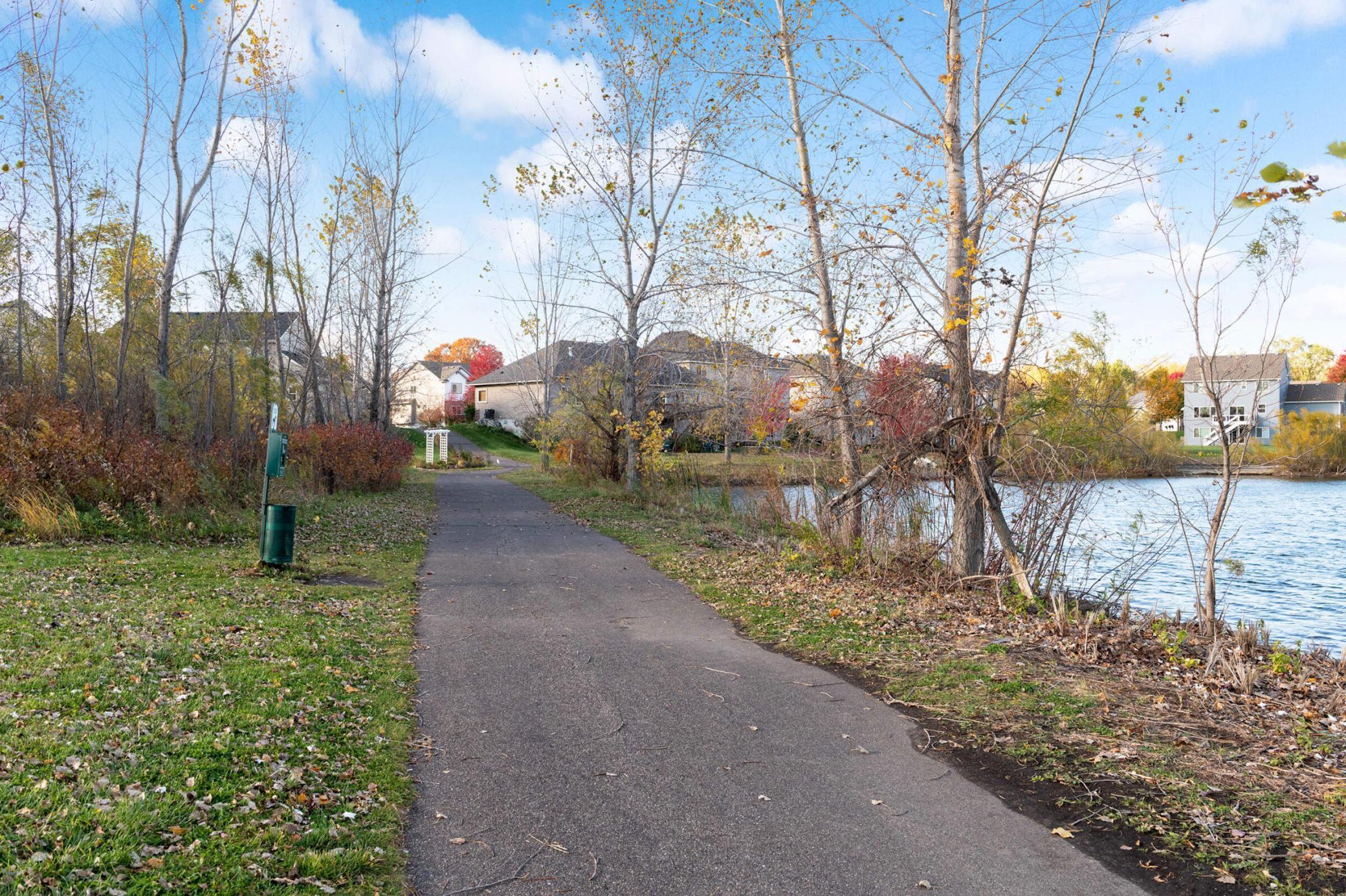 Neighborhood walking path beside a pond, with autumn trees and homes across the water.
