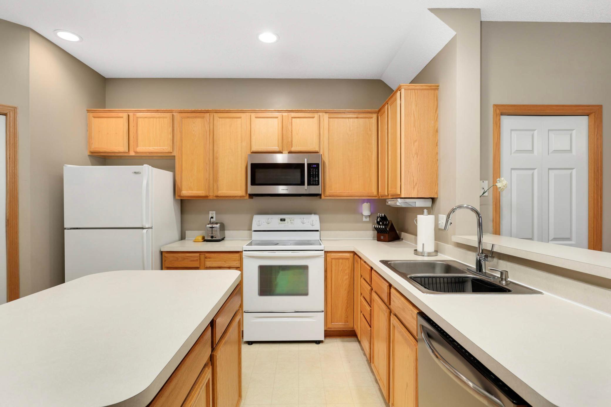 Kitchen with honey-colored cabinets, a foreground peninsula, and a double-basin sink.