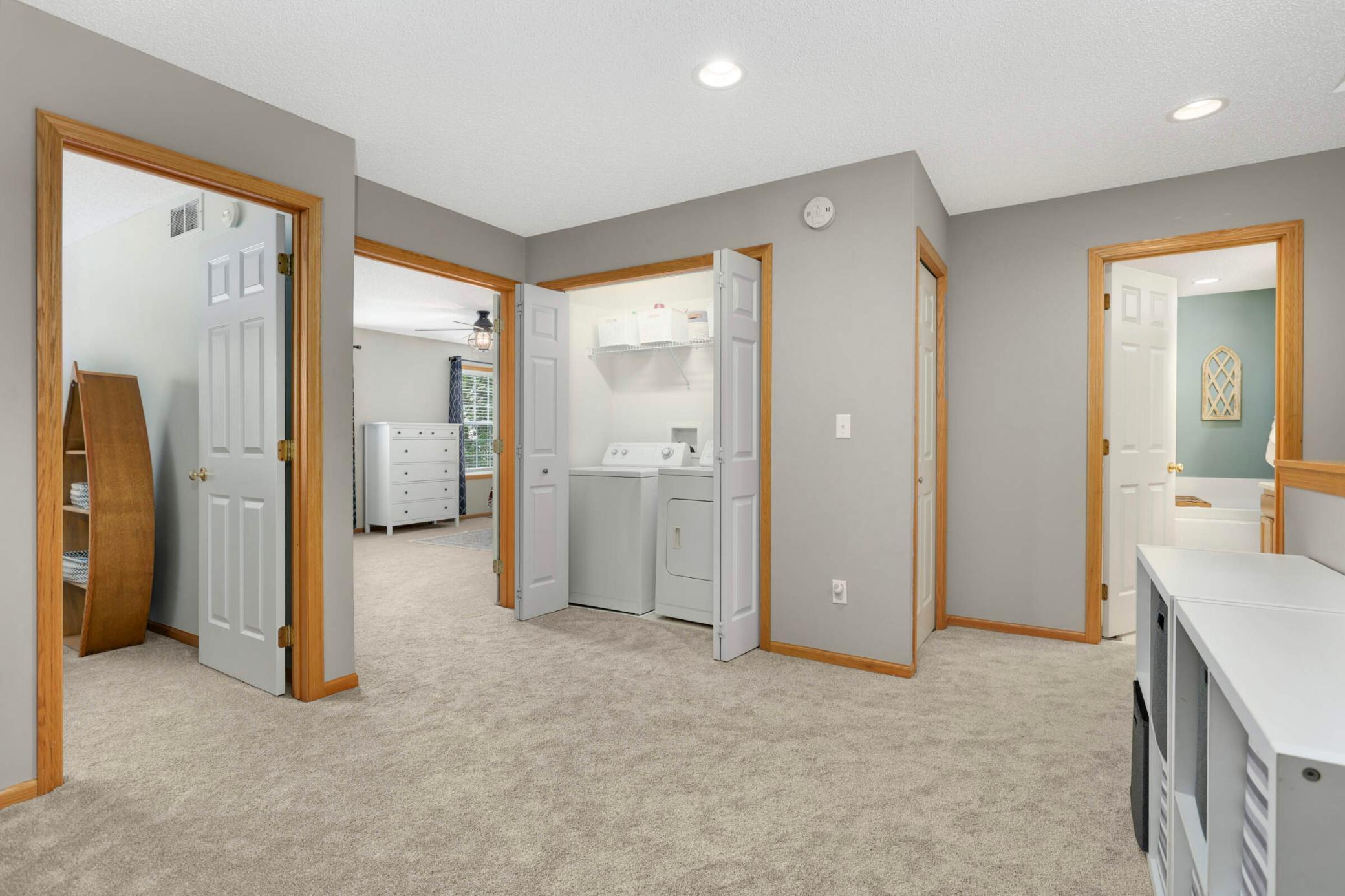 Carpeted hallway with an open washer-and-dryer closet and doorways to adjoining rooms.