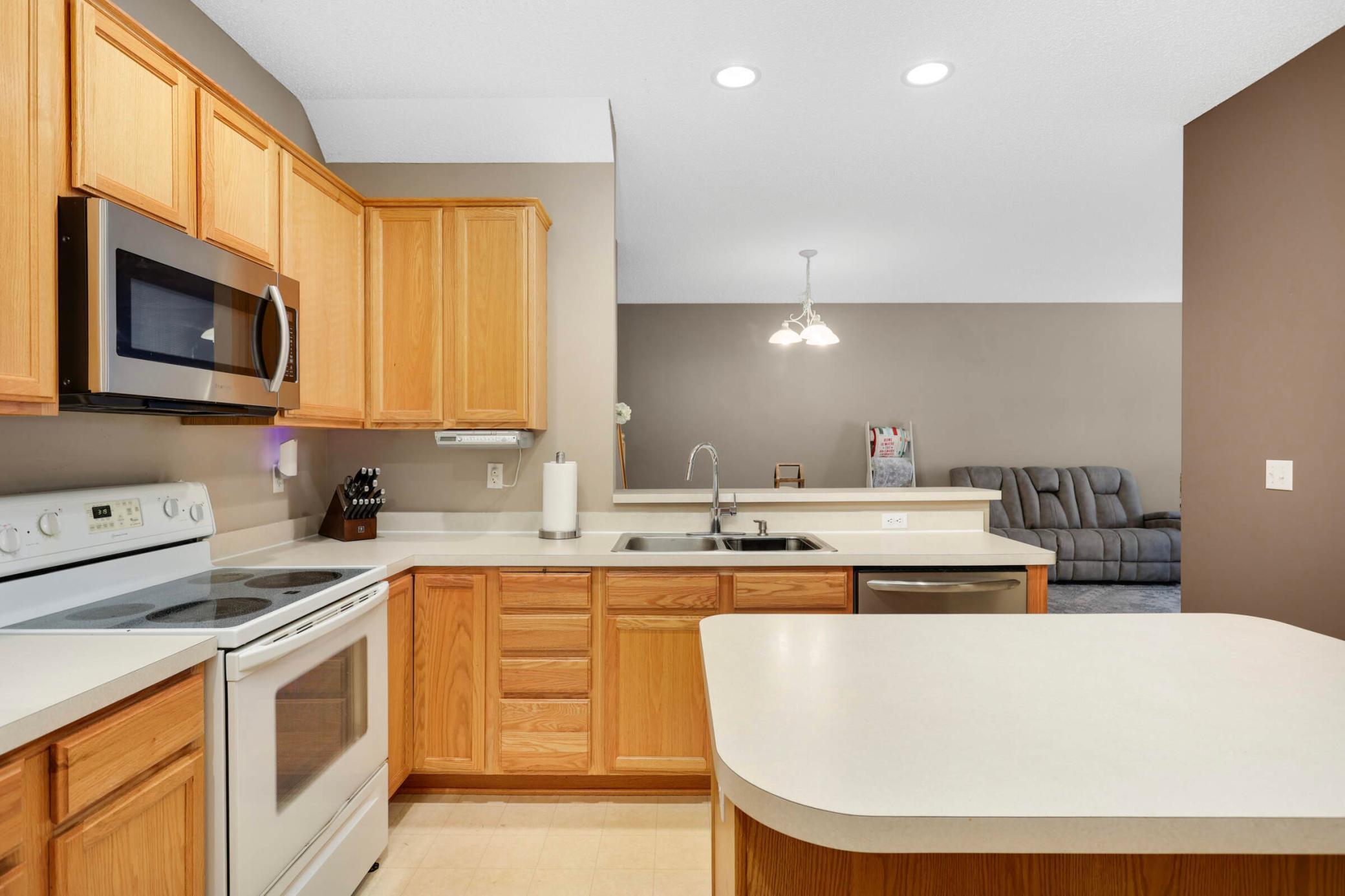 Kitchen with honey-colored cabinets, white appliances, a large peninsula, and a view into the living area.
