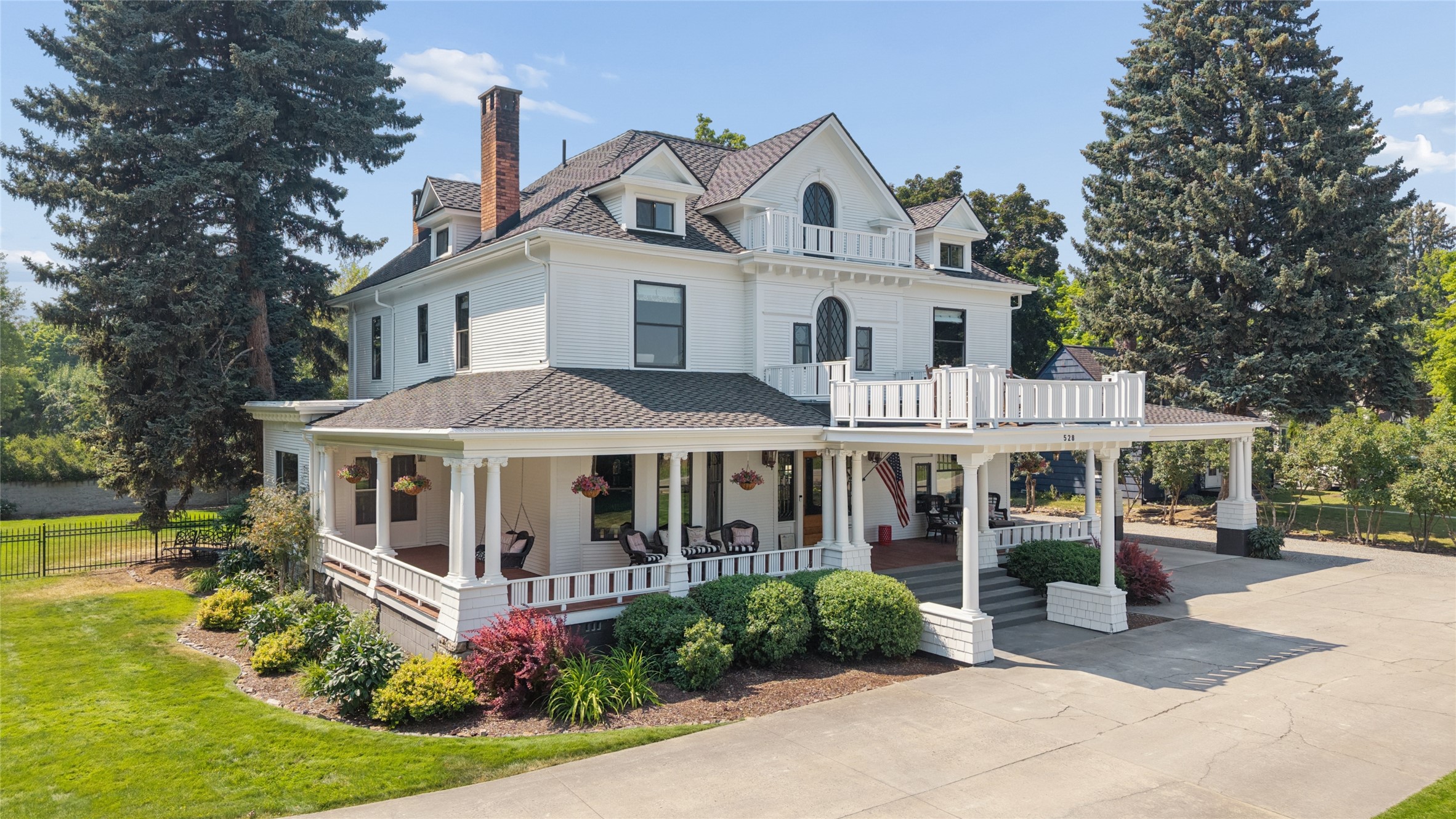 White Victorian-style house with a wraparound porch, hanging flower baskets, and landscaped lawn.