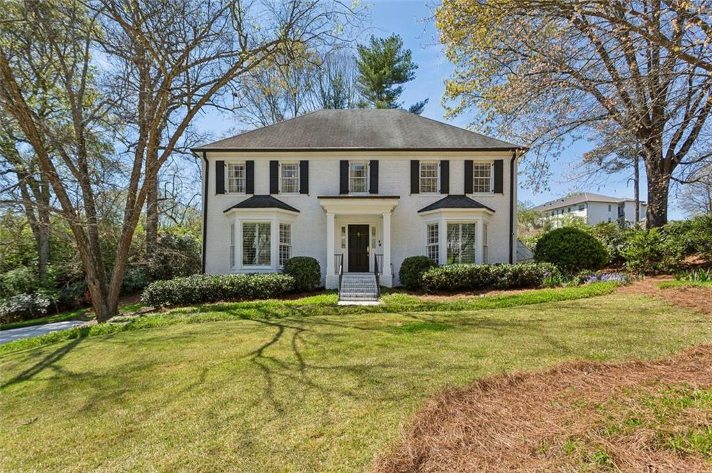Two-story white house with black shutters, bay windows, and a central entry behind a broad lawn.