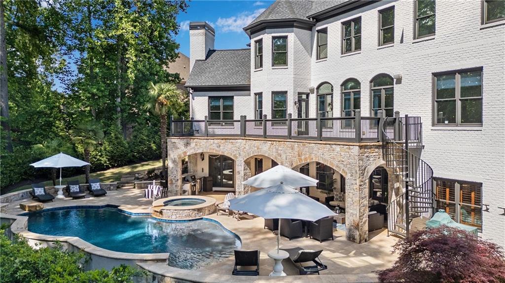 White brick home overlooking a pool and raised spa, with a stone-arched patio and spiral staircase.