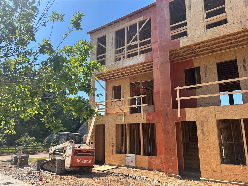 Multi-story home under construction with exposed wood framing and a Bobcat loader in front.