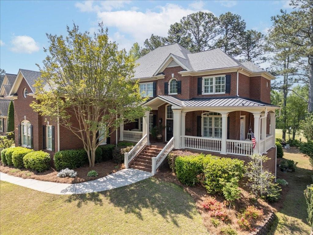 Two-story brick house with a white wraparound porch, front steps, and landscaped yard.