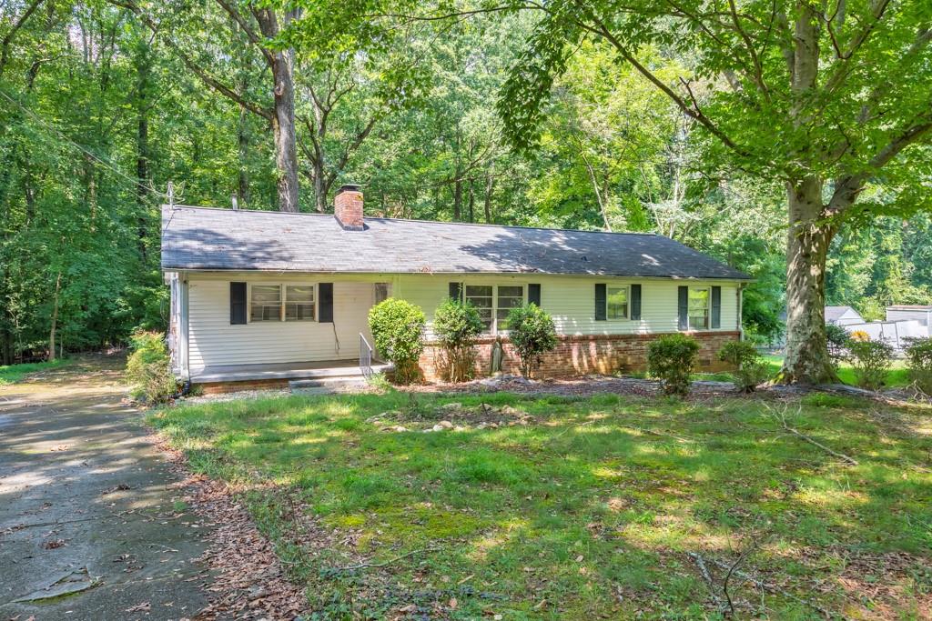 Ranch-style house with a brick lower facade, shaded by mature trees beside a paved driveway.