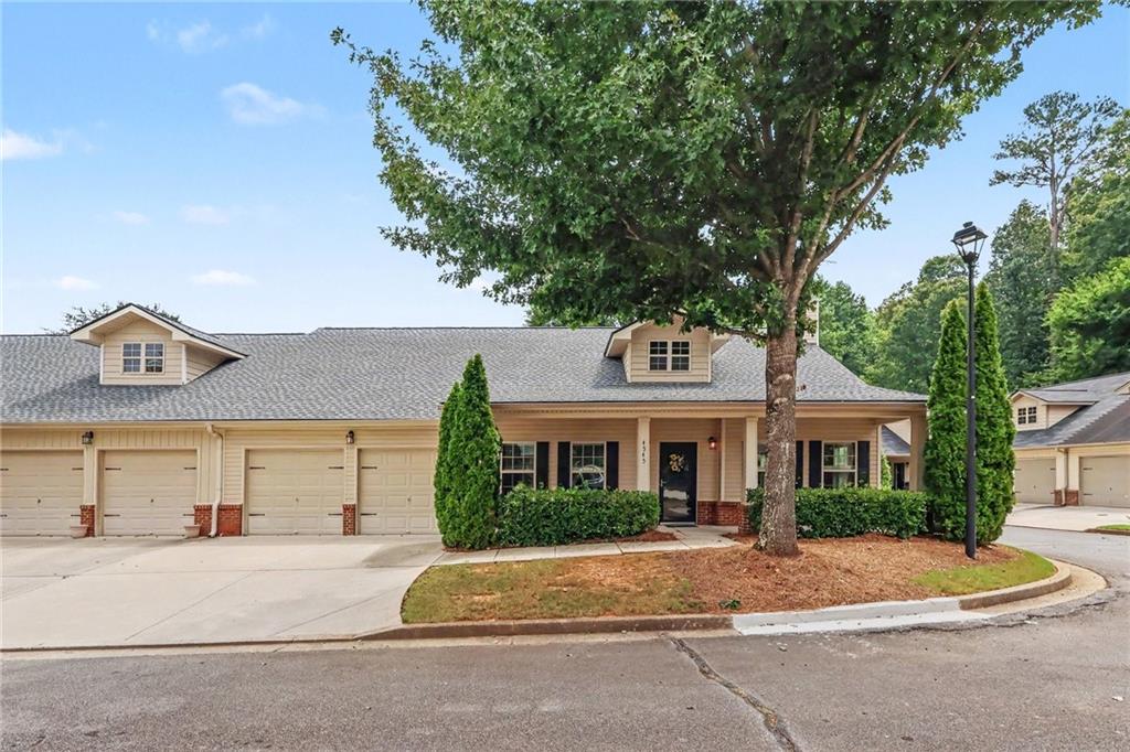 Beige attached home with multiple garage doors, a covered entrance, and a large shade tree.