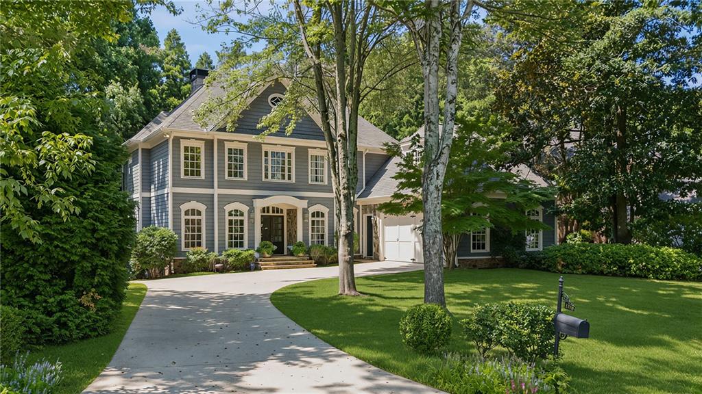 Gray two-story house with white trim, a curved driveway, and mature trees.