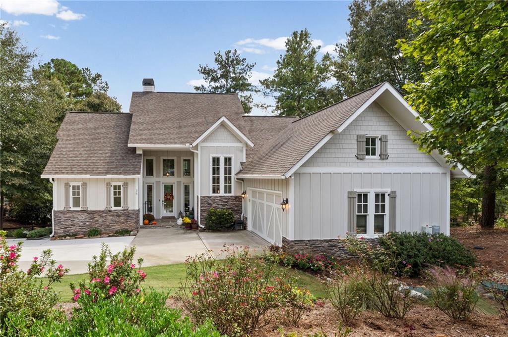 White two-story house with stone accents, a wide driveway, and landscaped flower beds.